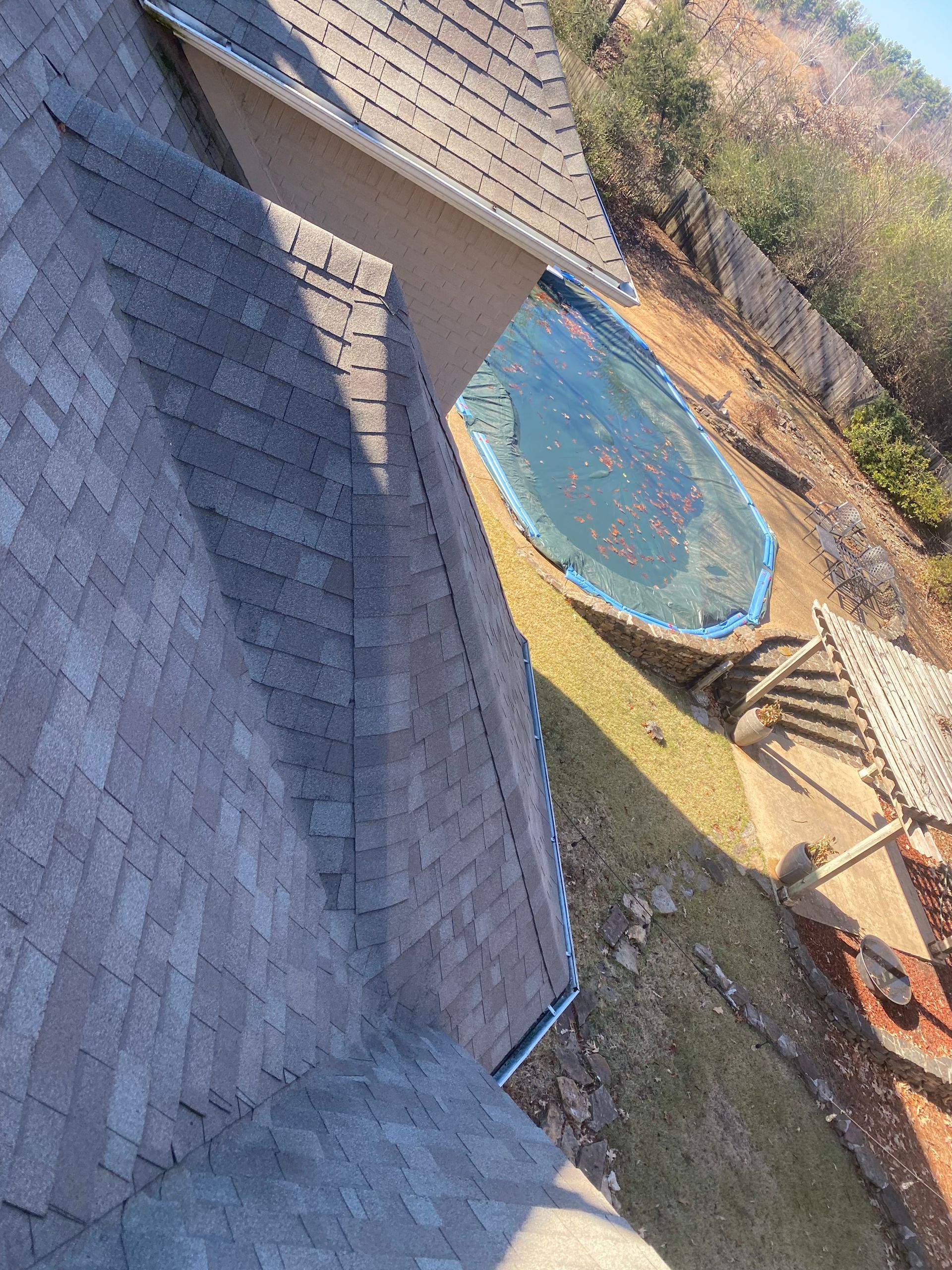 A house with a gray shingle roof next to a backyard with a covered pool and a pergola on a sunny day.