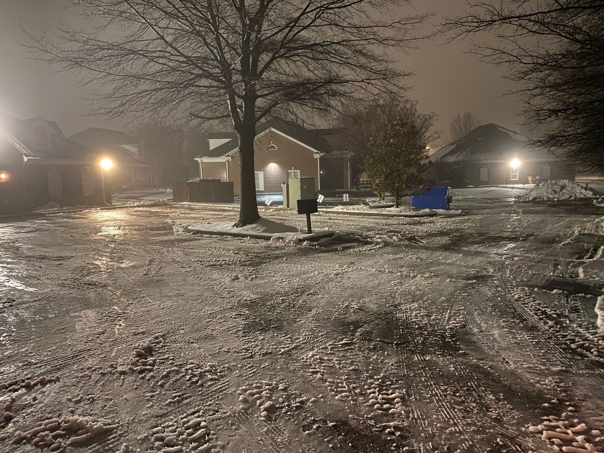 Icy residential street at night, covered in ice and snow.  Streetlights illuminate houses, fog in the background.
