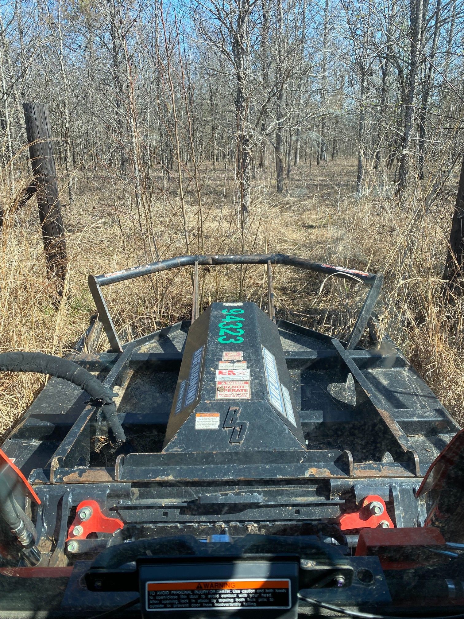 View from a brush cutter clearing a path through dry brush and trees in a wooded area.