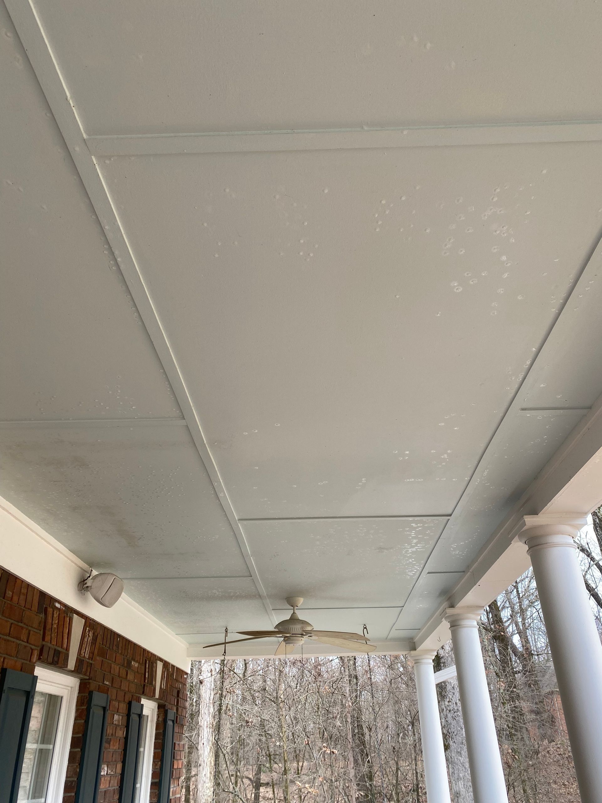 White porch ceiling with paneling and a ceiling fan, supported by brick and white columns.