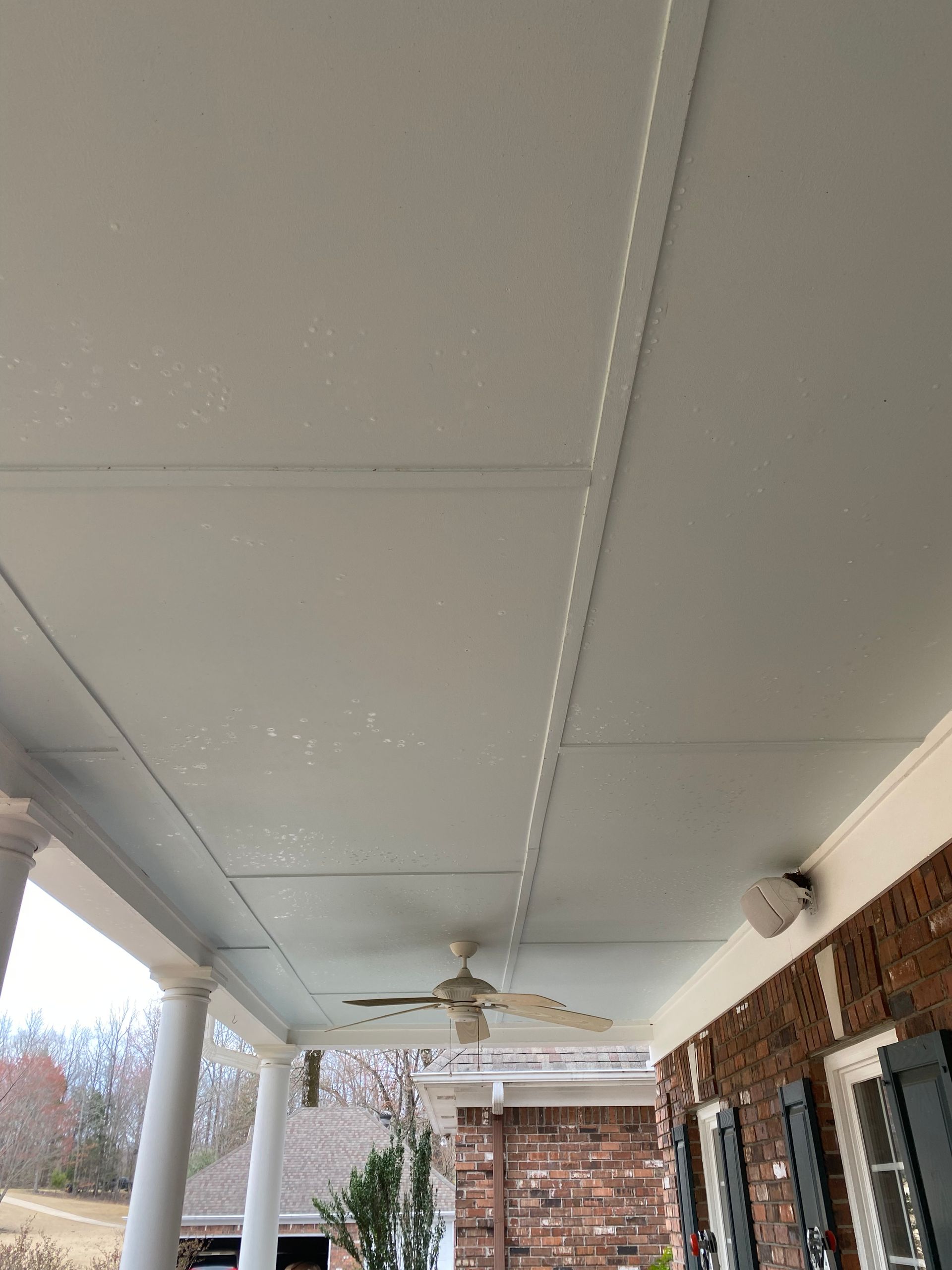 White porch ceiling with a ceiling fan, a speaker, and molding against a brick wall.
