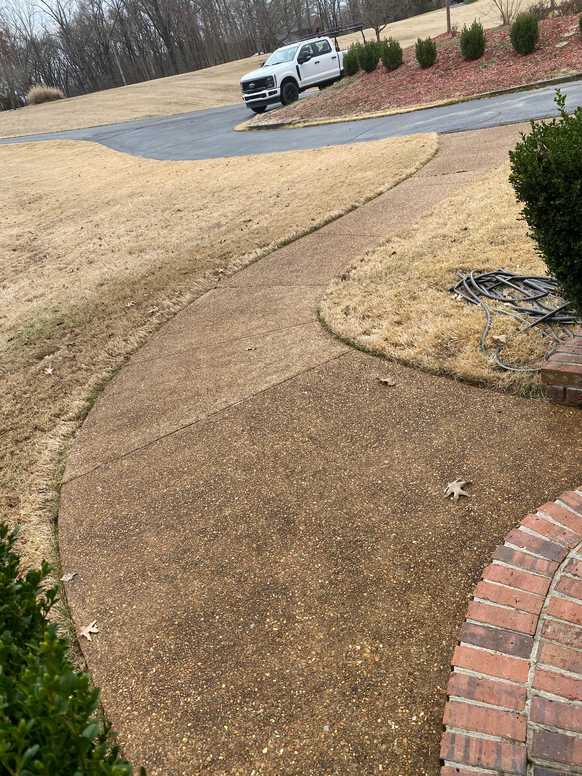 Gravel walkway curves towards a driveway where a white truck is parked. Dry grass and brick details are also visible.