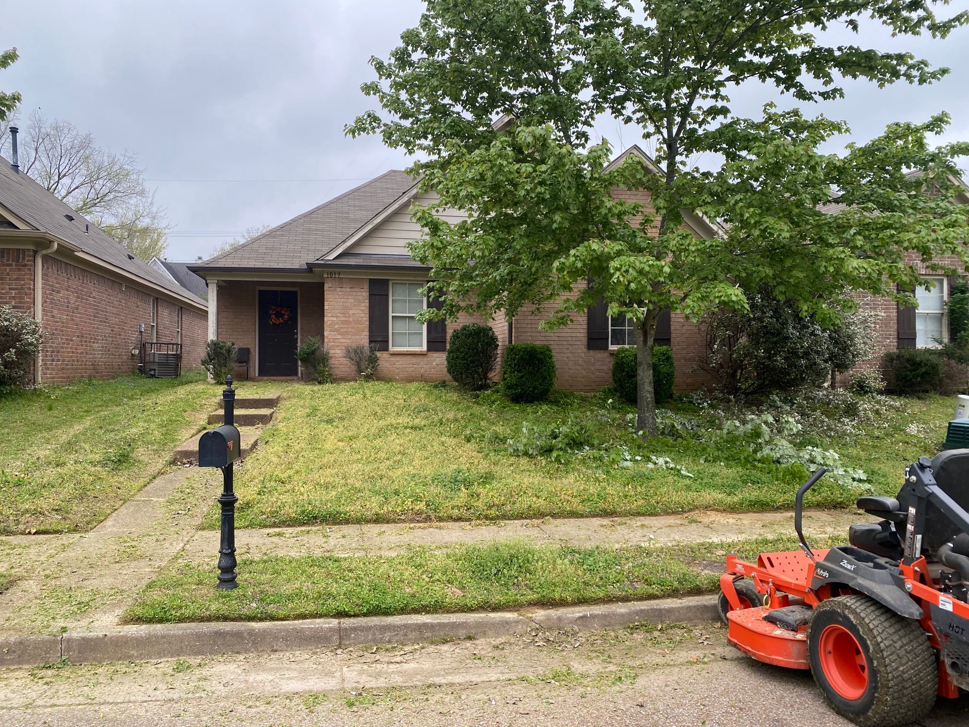 A brick house with a lawn being mowed. A black mailbox is in front of the house. An orange riding mower is on the right.