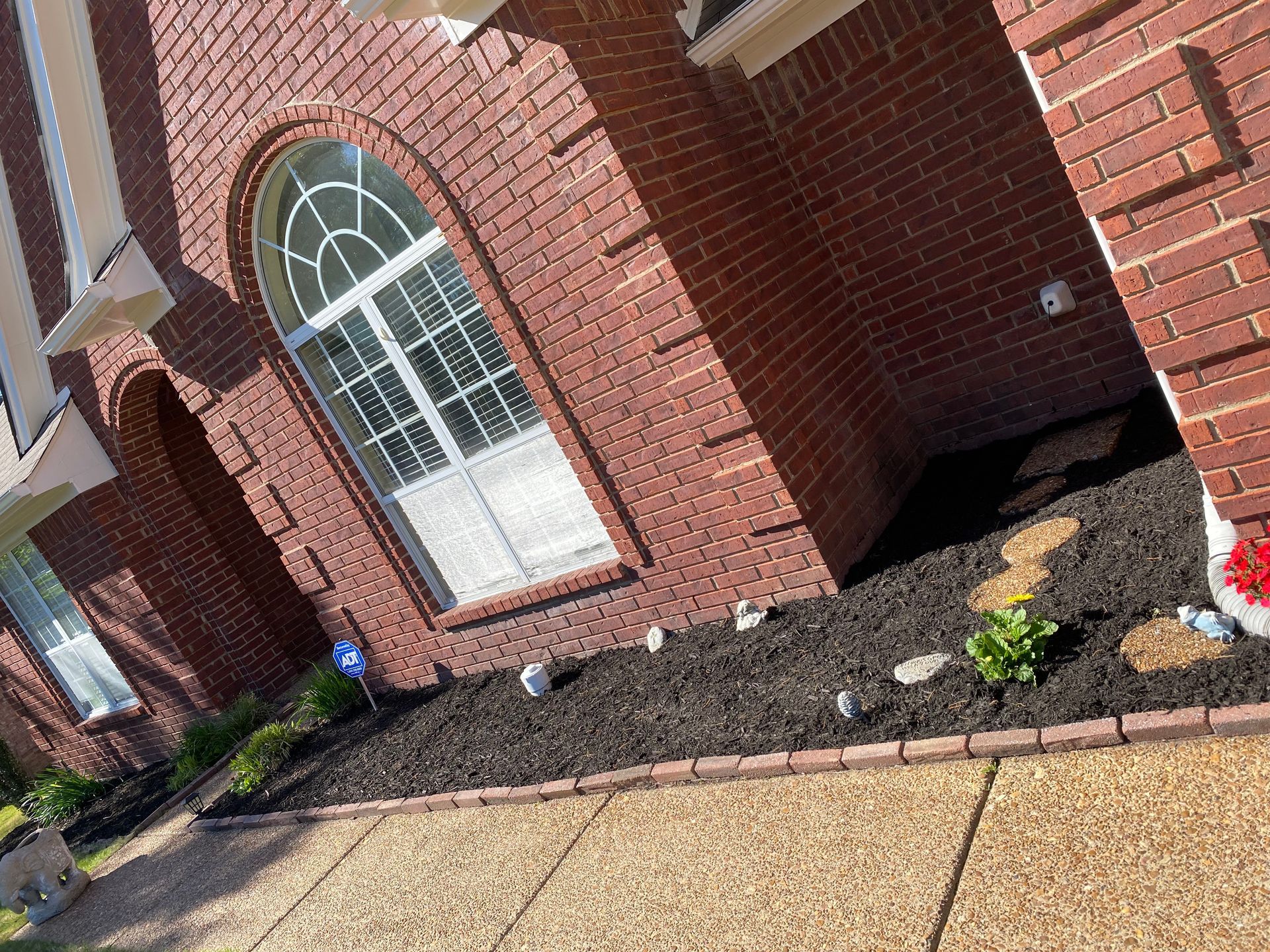 Brick house exterior with arched window, dark mulch, and paved walkway.