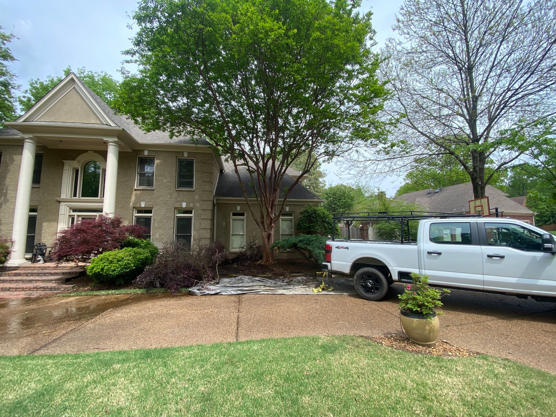 A large two-story brick house with white columns, landscaping, and a white pickup truck parked in the driveway.