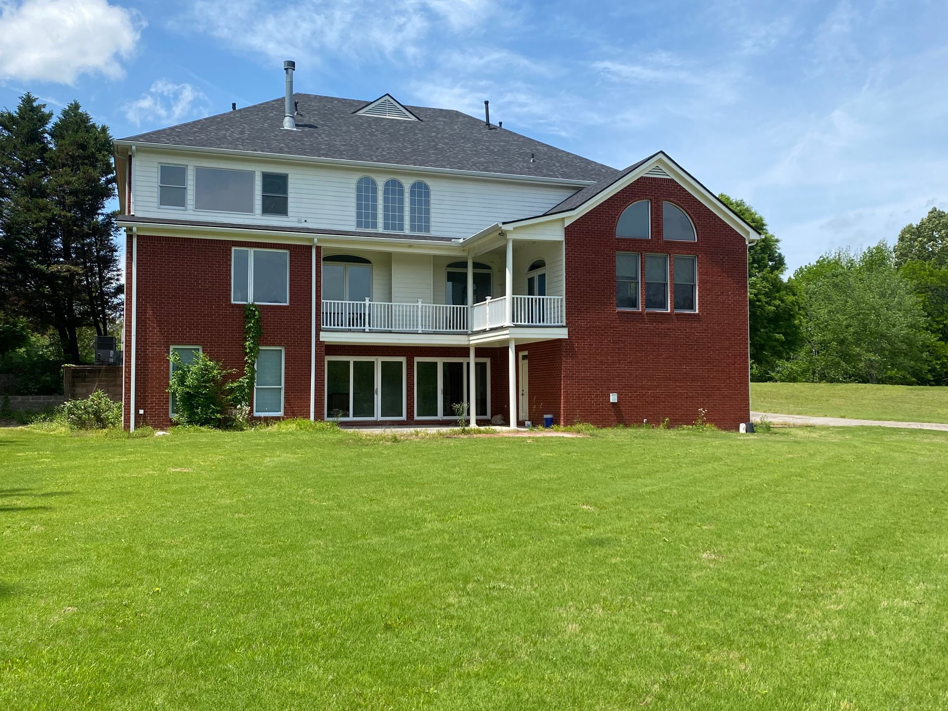Two-story brick and white house with a large green lawn under a blue sky with trees.