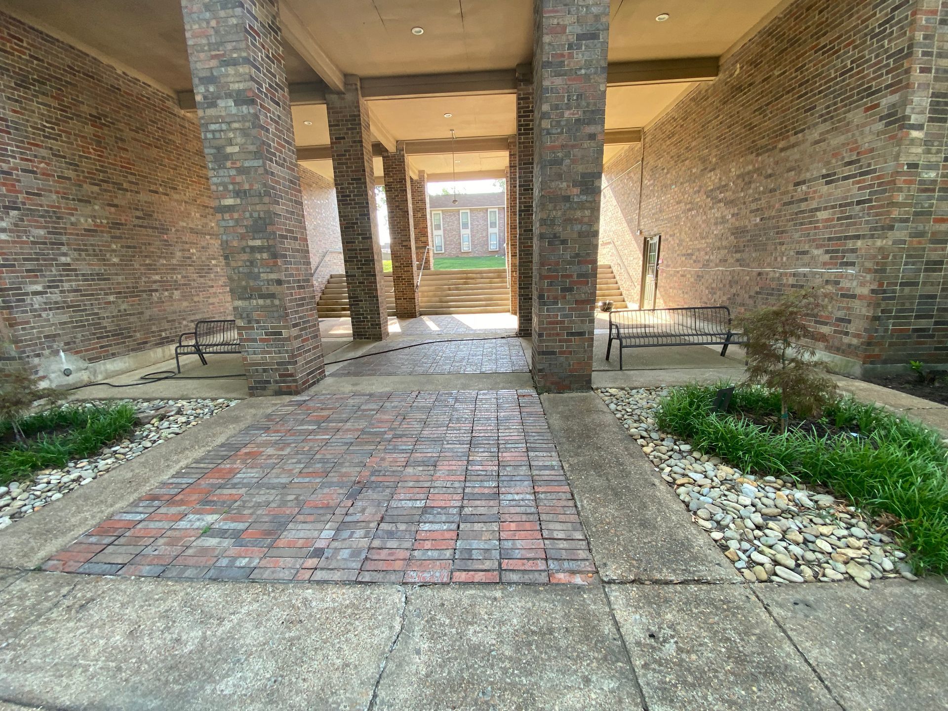 Brick and concrete entranceway with columns, steps in the distance, and small plants in the foreground.