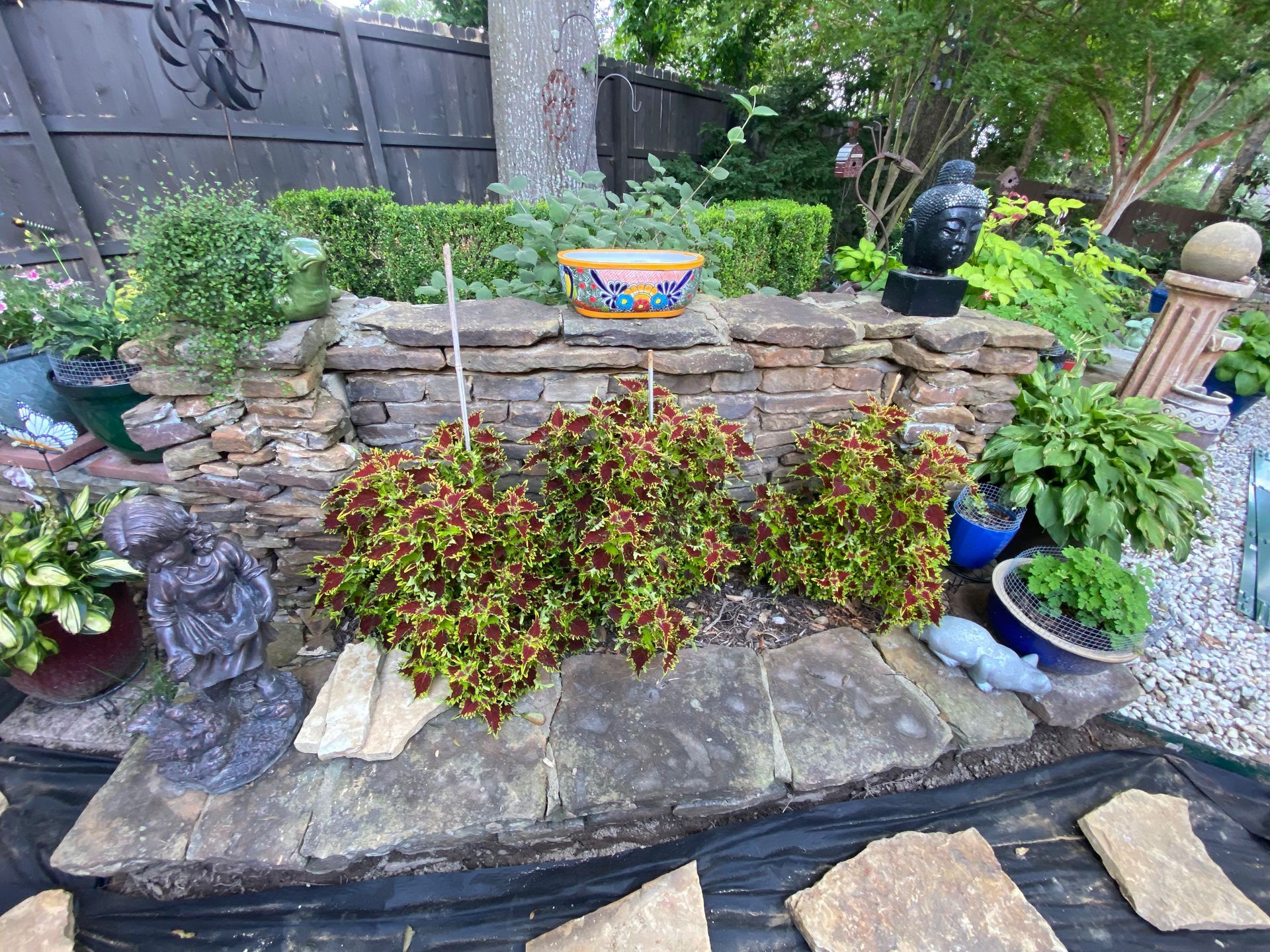 A tiered garden bed with coleus plants in the foreground, stone edging, and a decorative pot.