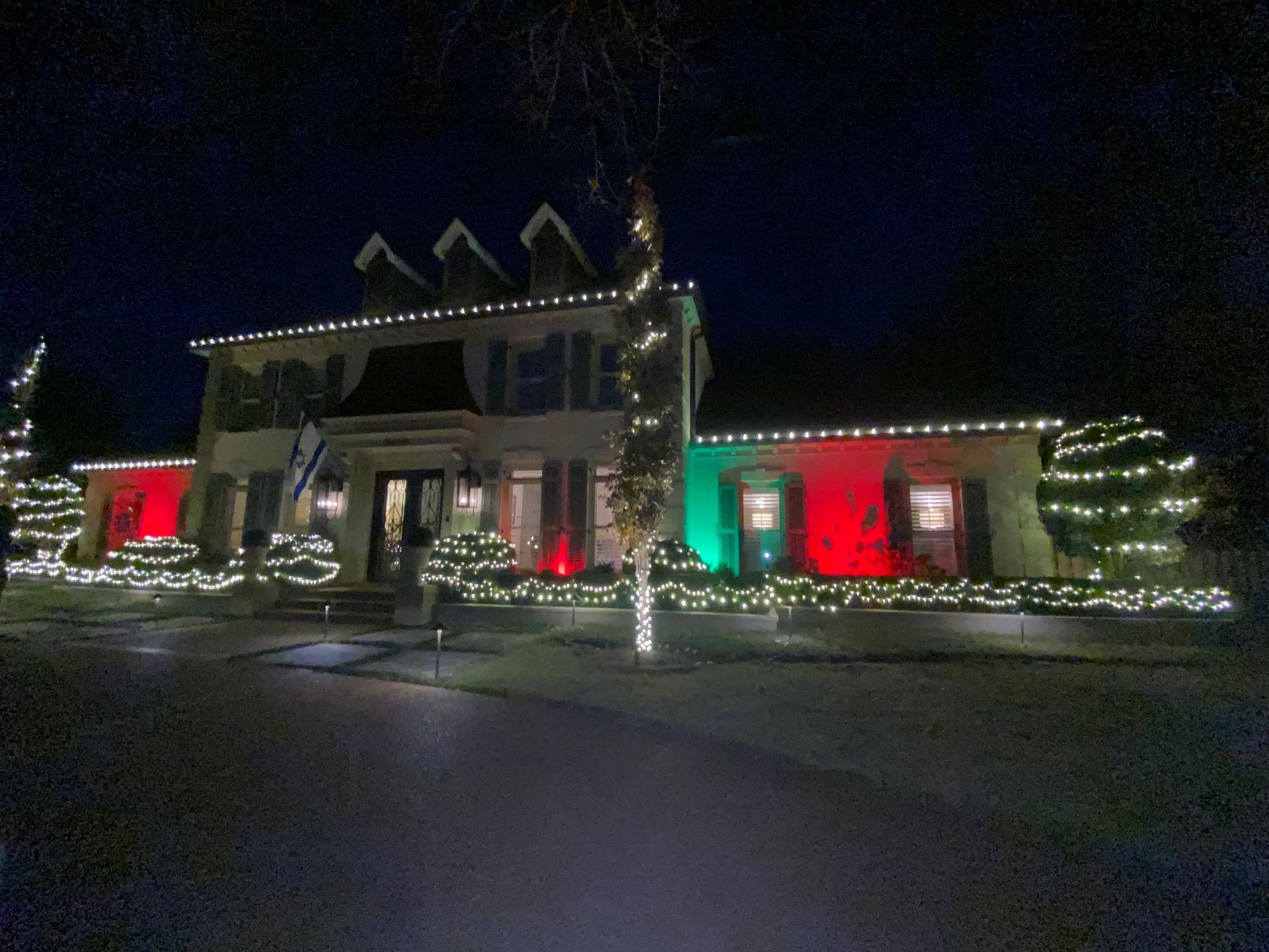 A two-story house decorated with white Christmas lights. Sections of the house are lit with red and green lights.