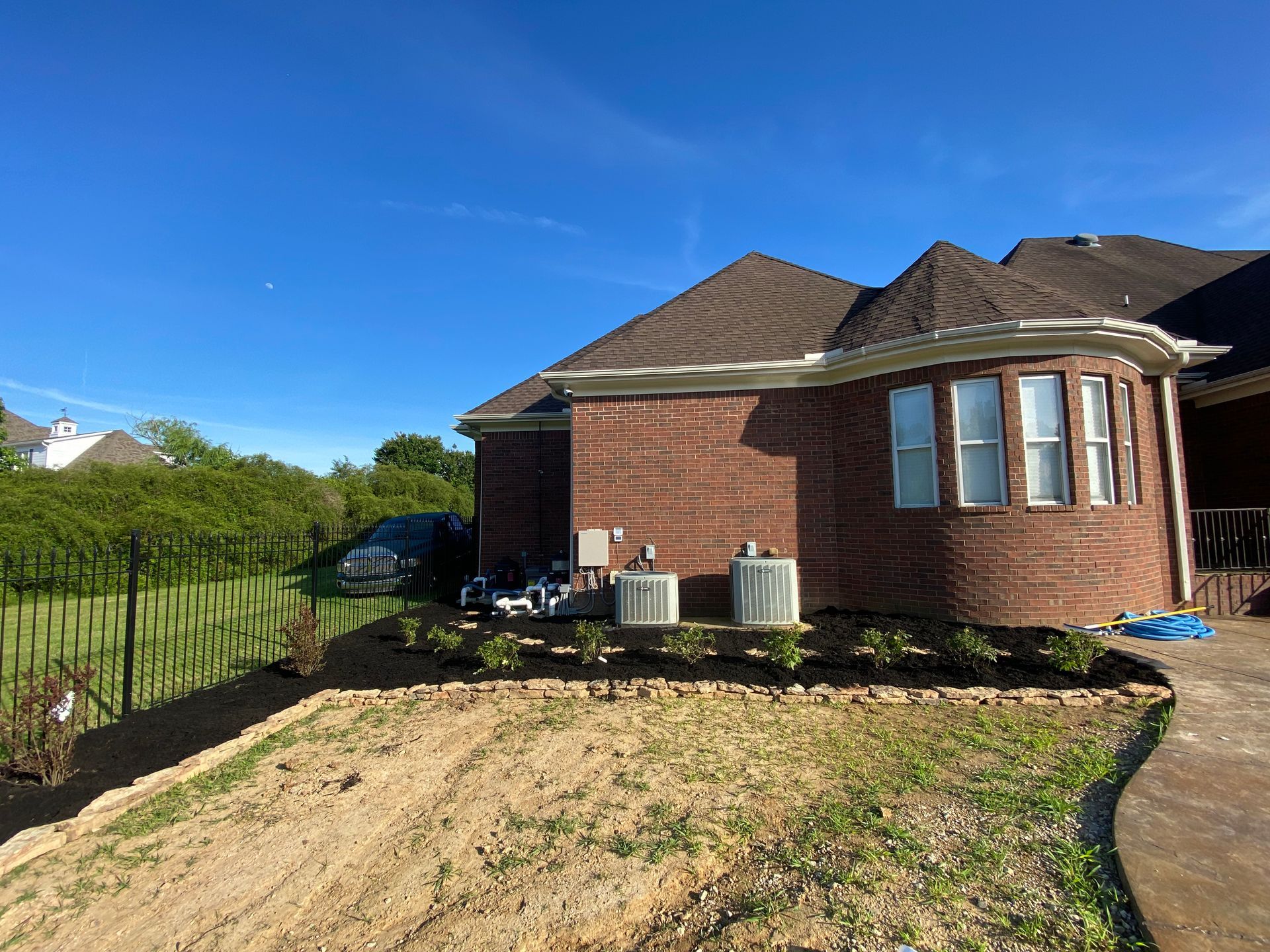 Brick house with air conditioning units and landscaping under a bright blue sky.