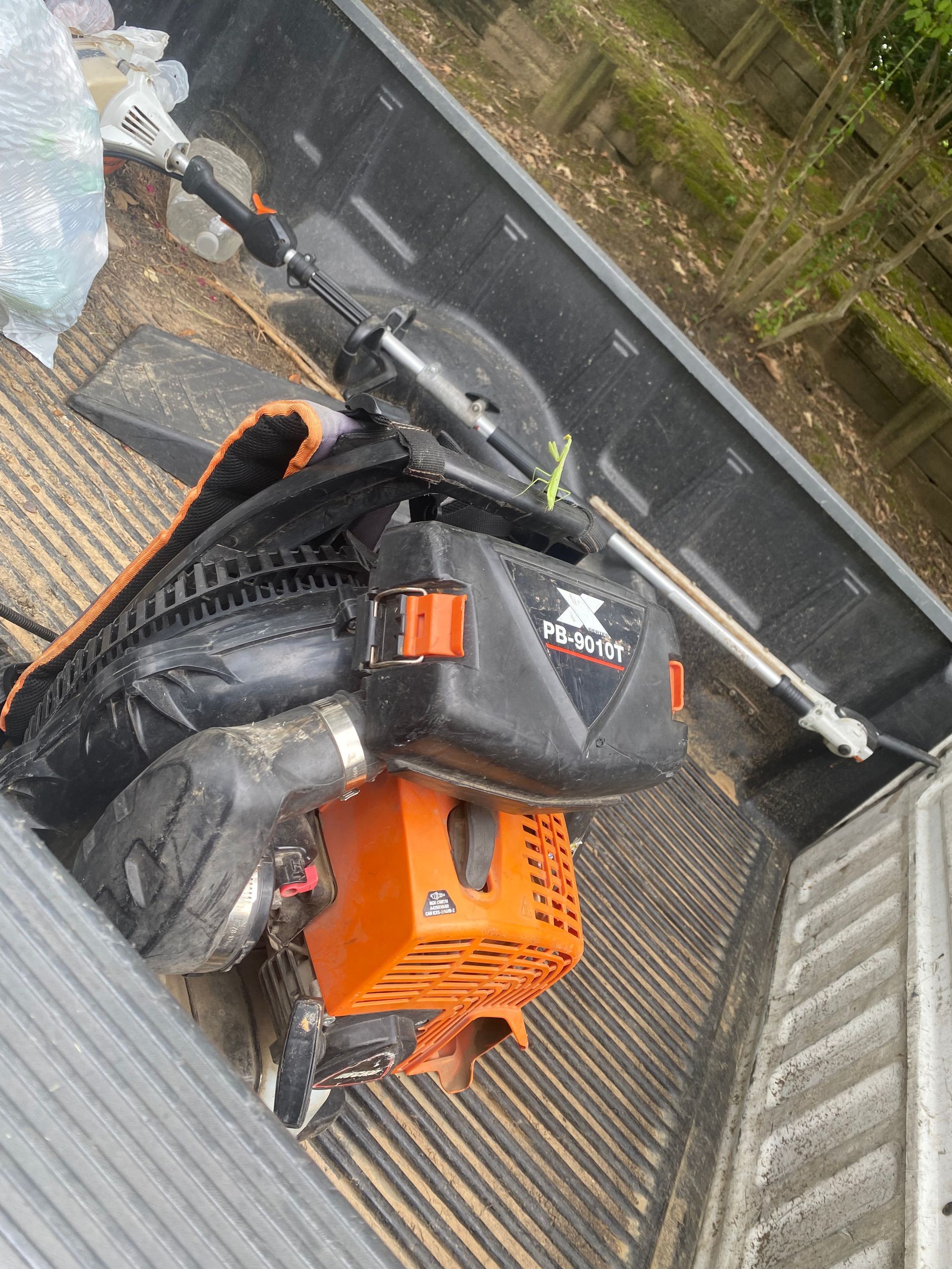 A gas-powered weed whacker in the bed of a truck. The motor is orange and black.