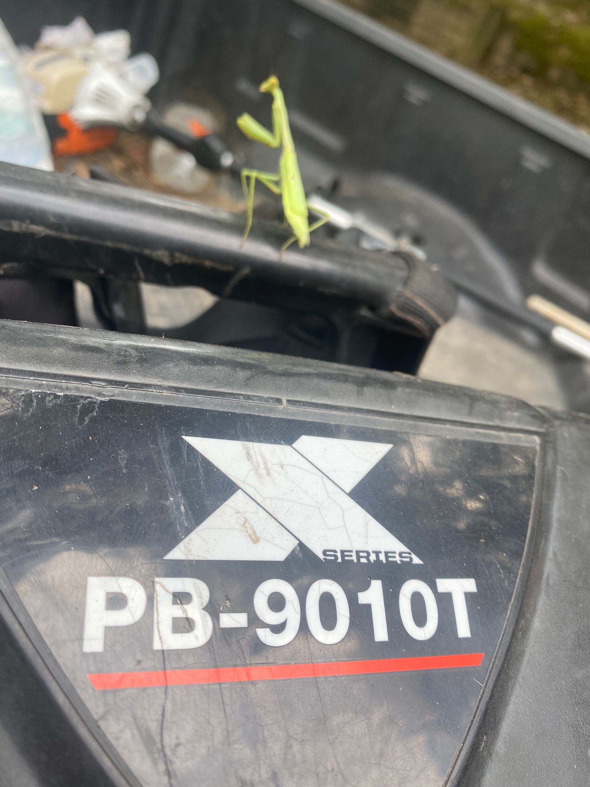 Green praying mantis perched on a black machine, with the text 