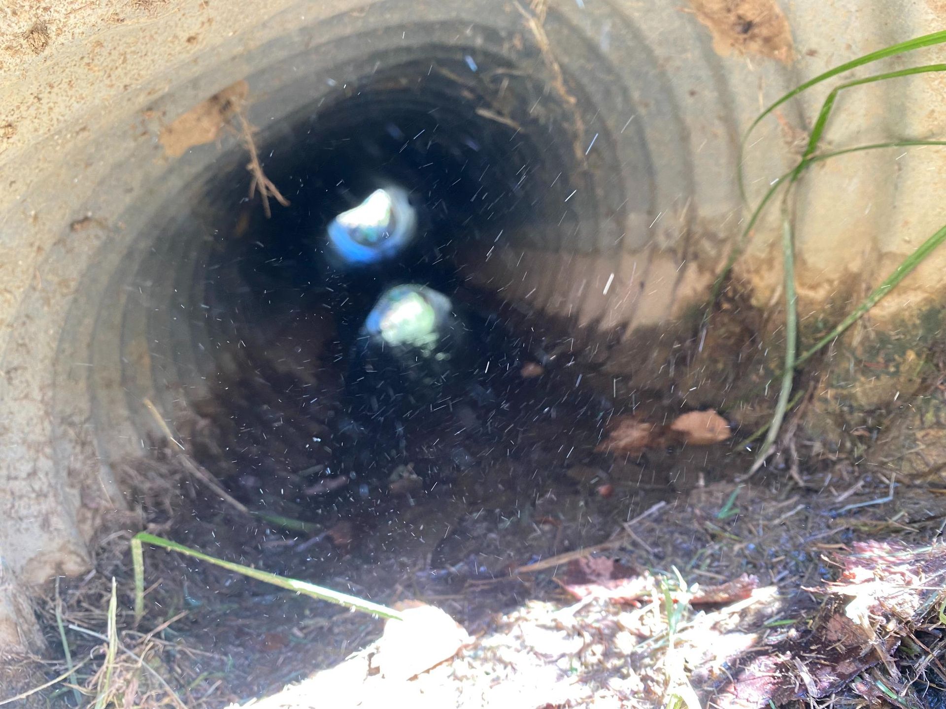 Looking into a corrugated metal culvert. Dark interior with two bright, round spots visible in the distance.