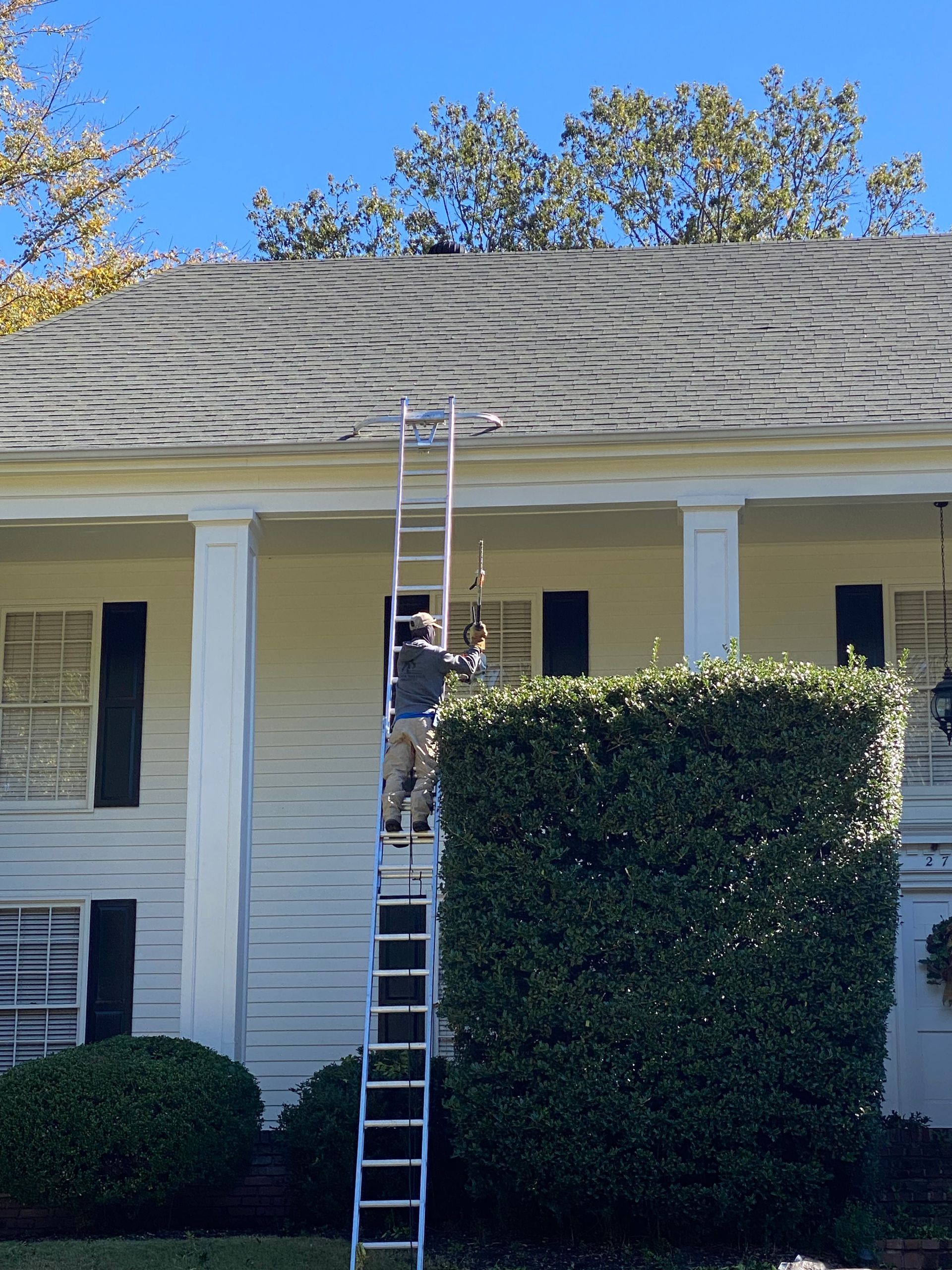 A person climbs a tall ladder to access a roof on a two-story white building with a blue sky.