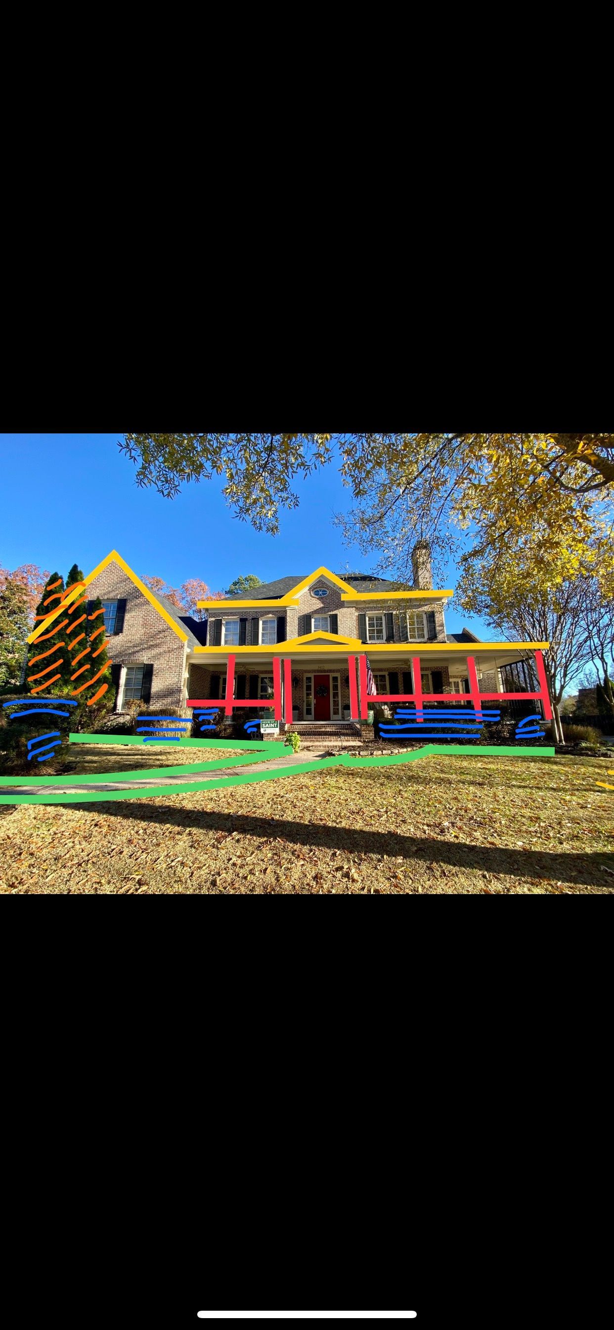 Large house with a wraparound porch. Fall foliage and a blue sky surround the building. The porch trim is painted red and blue.