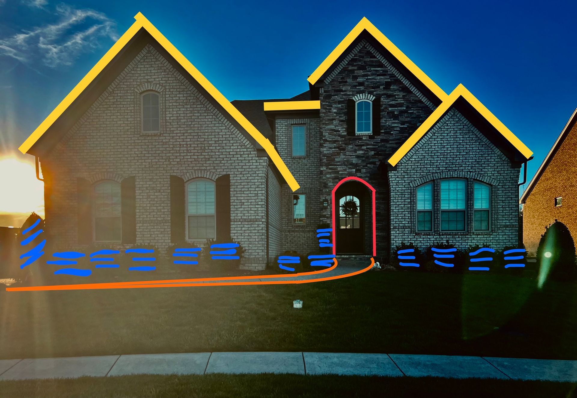 A house with a brick facade and yellow roof accents sits on a green lawn. Blue lines outline possible landscaping and a path.