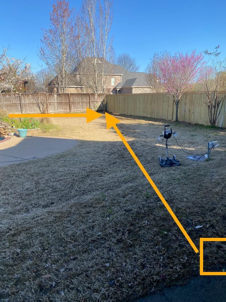 Backyard with brown grass and a wooden fence under a blue sky. An arrow points from the lower right corner to the middle of the fence.