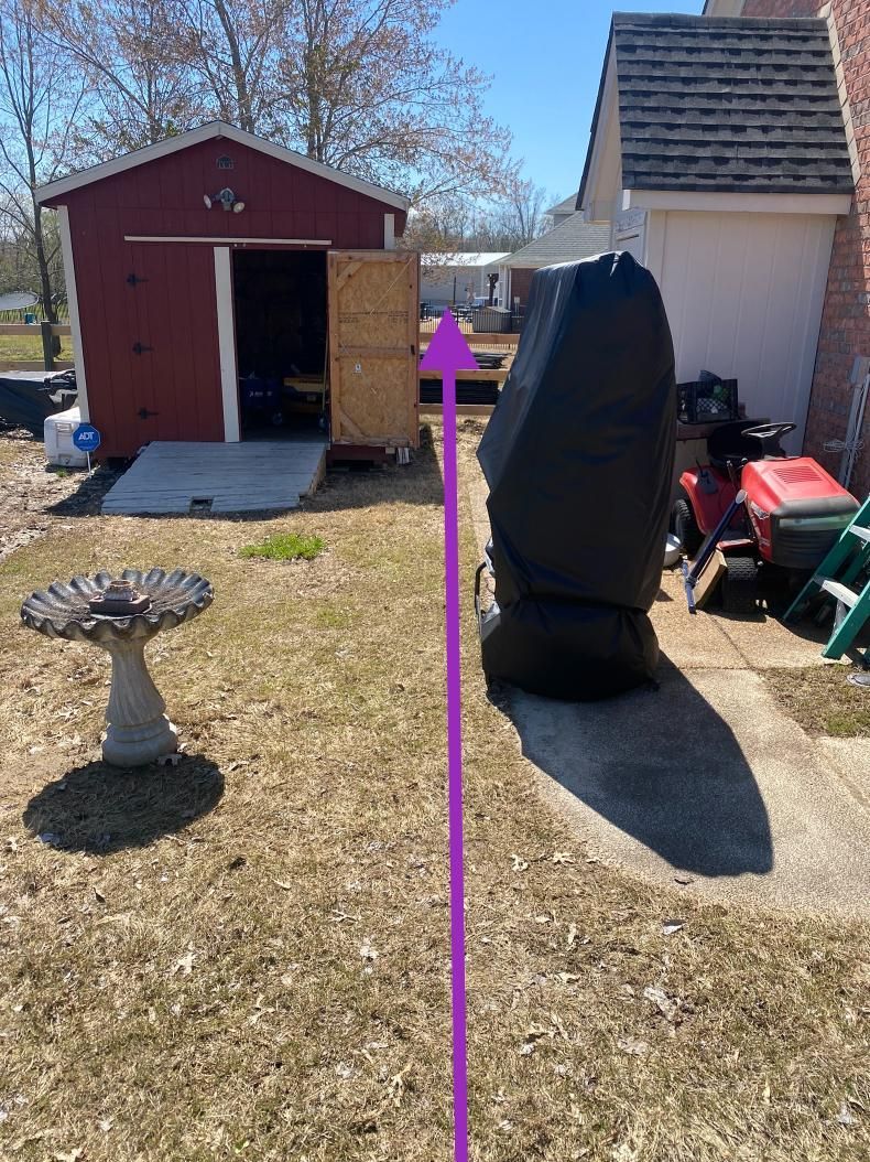Backyard scene with a red shed, a covered object casting a shadow, and a birdbath. A purple arrow indicates the space between them.
