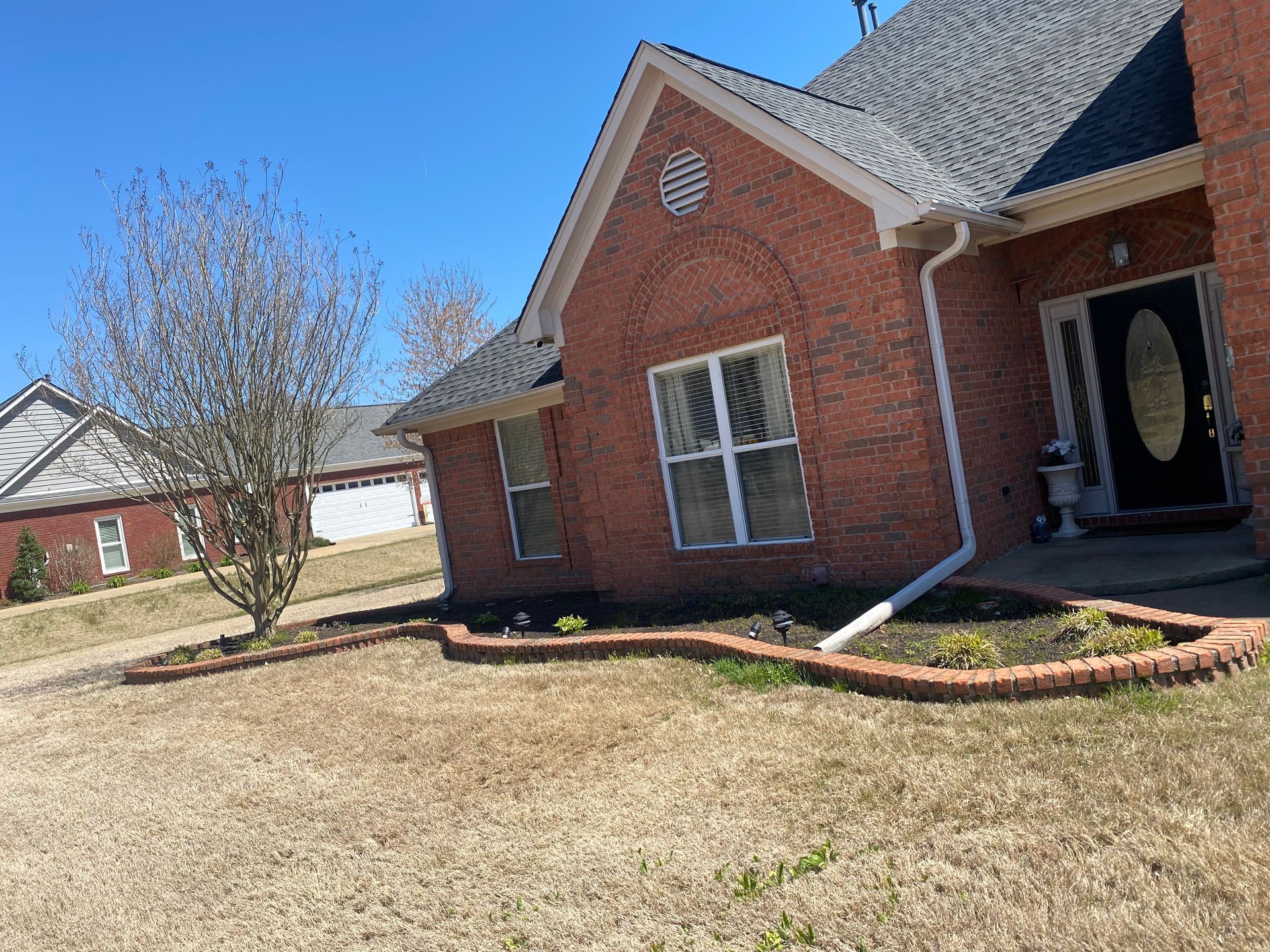 Red brick house with a landscaped yard and bare tree in front. Blue sky background.