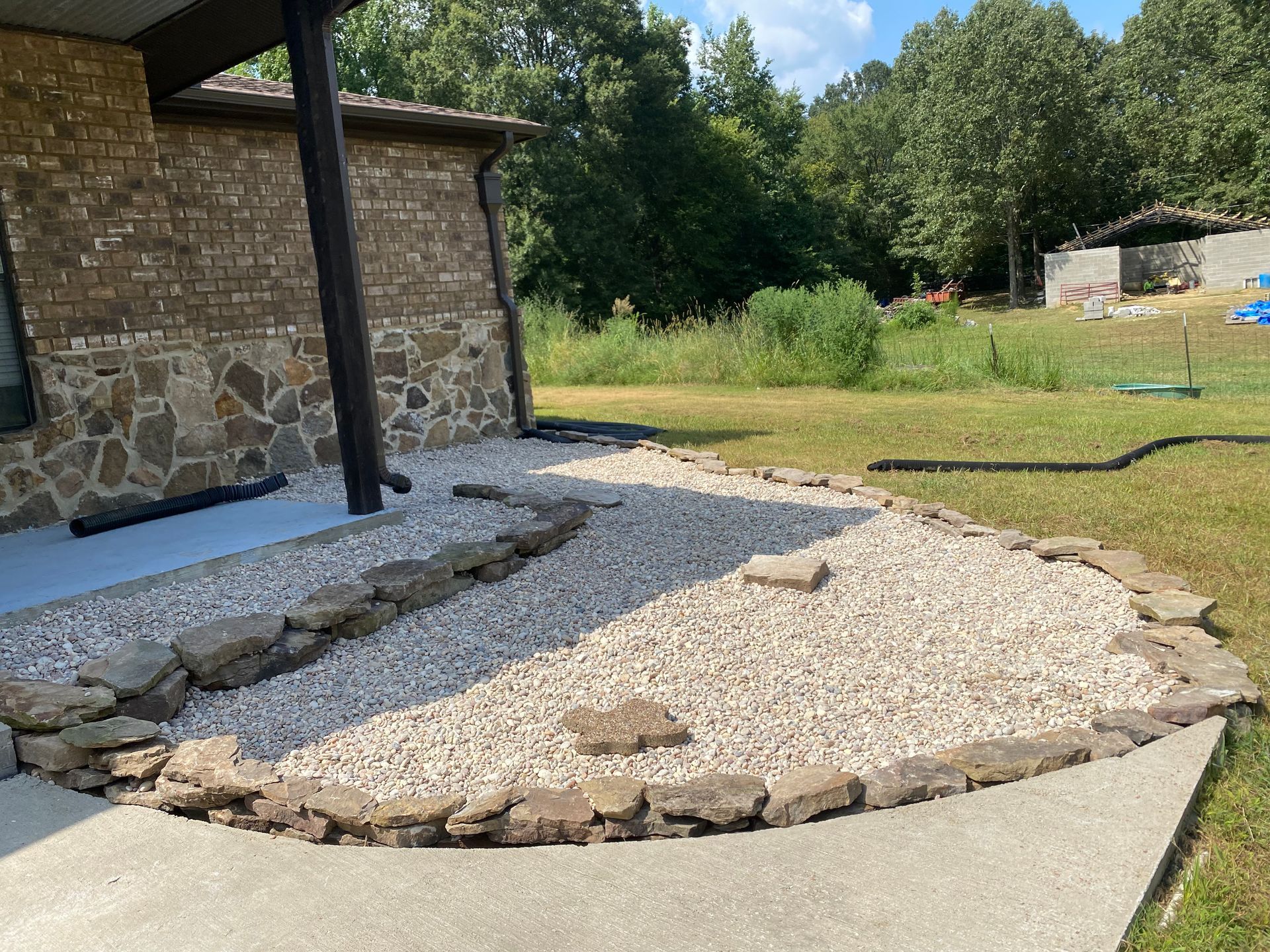 Side view of a building with a stone and brick facade, gravel landscaping, and a concrete walkway bordered by rocks.