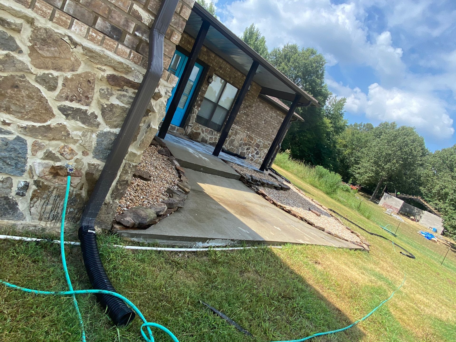 A house with a stone facade and a concrete walkway leading to a blue door. A black awning shades the entrance.