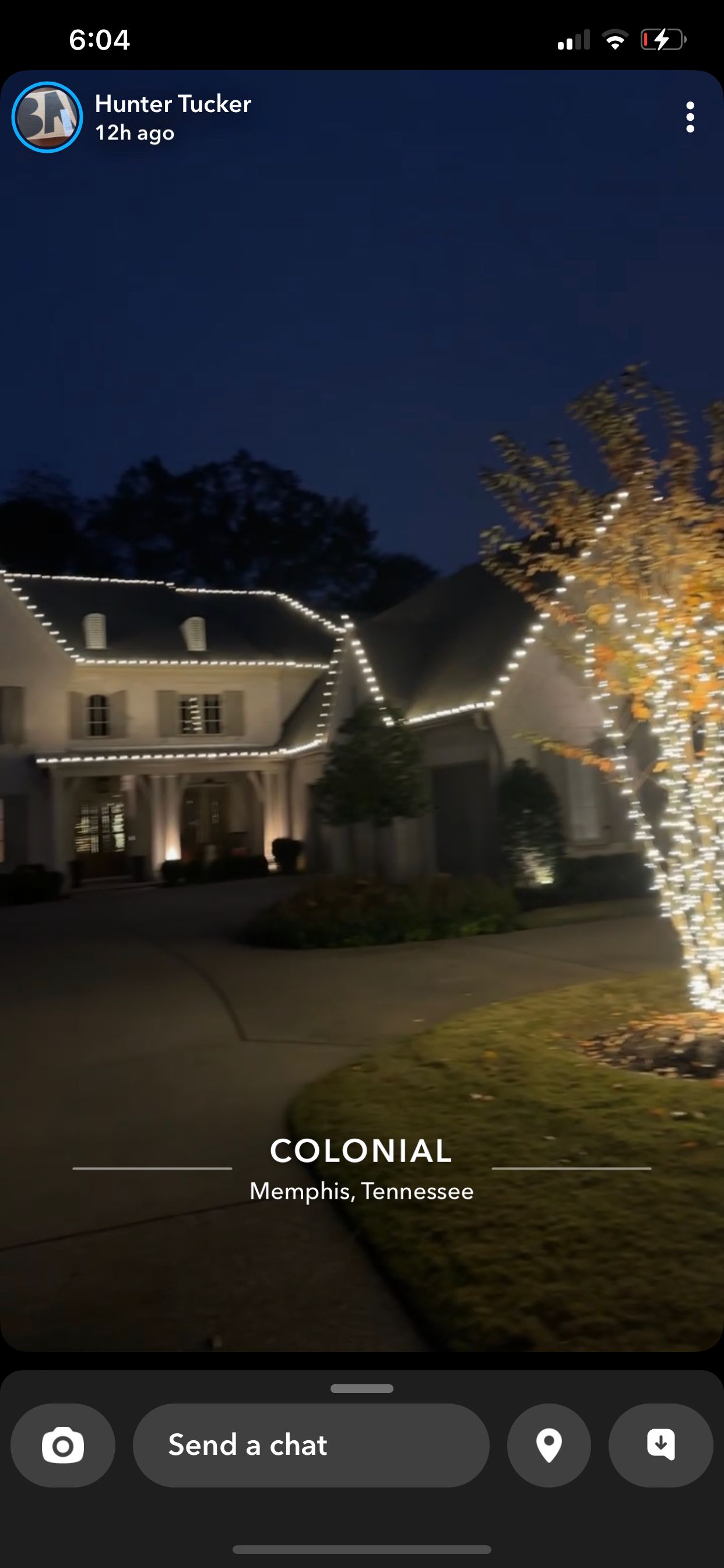 A nighttime shot of a colonial-style house with Christmas lights. The house is well lit, with lights outlining the roof and wrapping a tree.