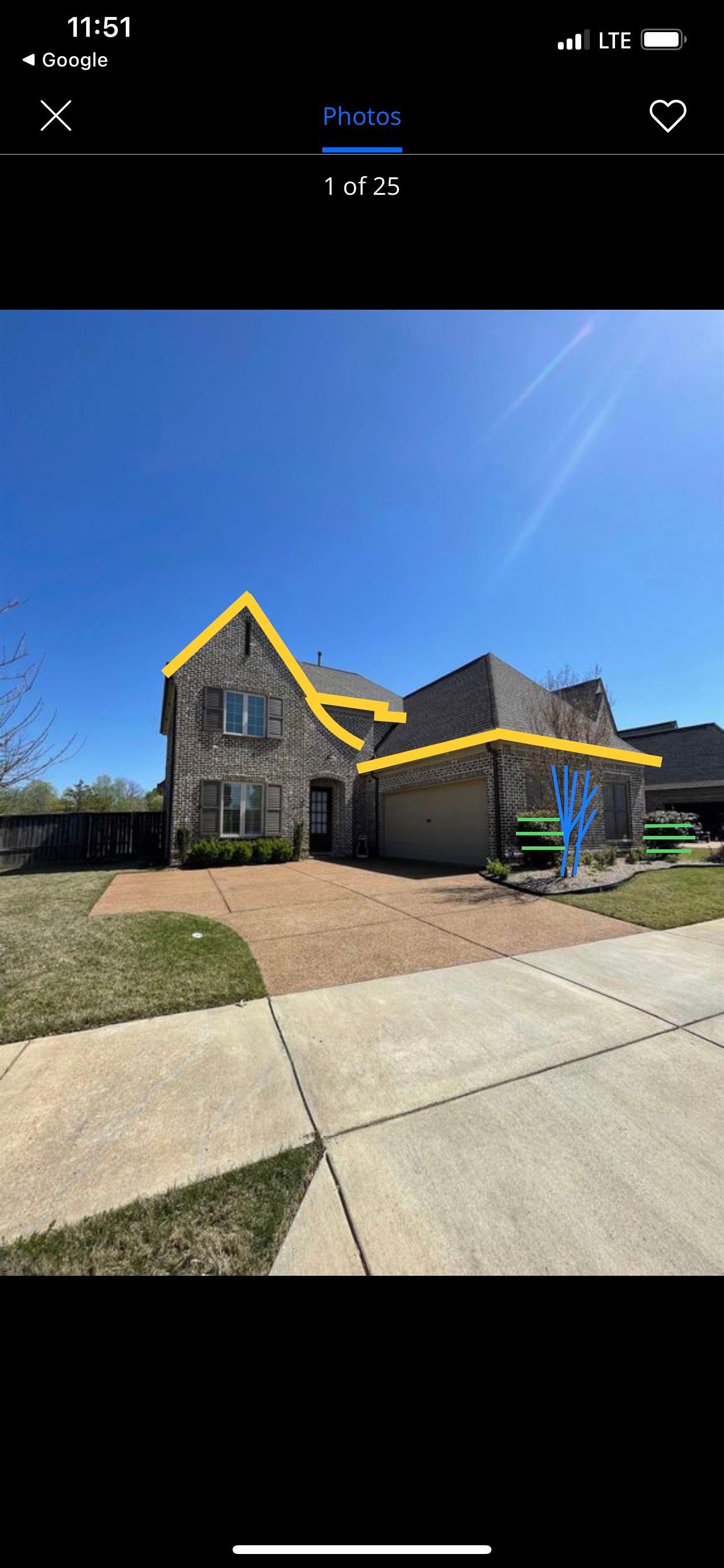 A stone-faced house with a brown driveway and green lawn under a bright blue sky.