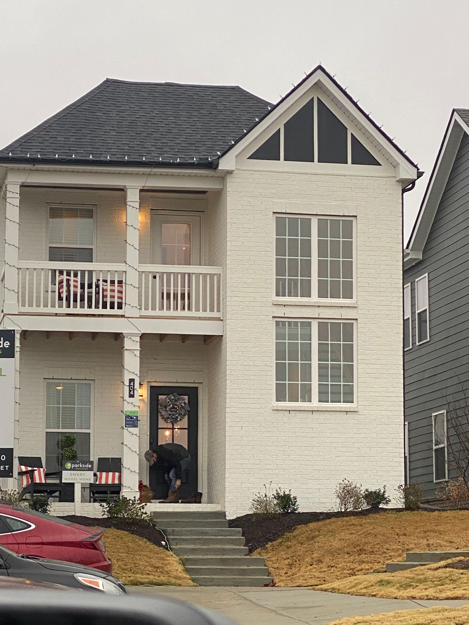 Two-story white brick house with black roof, porch, and steps leading to the front door. A person is by the entrance.