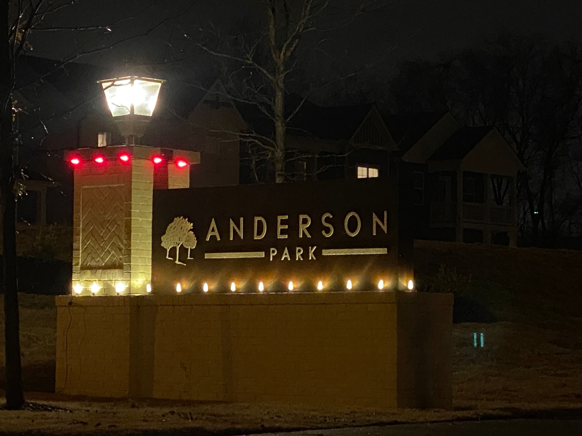 Anderson Park sign lit up at night with festive lights. The sign is brown, and red and white lights outline the top.