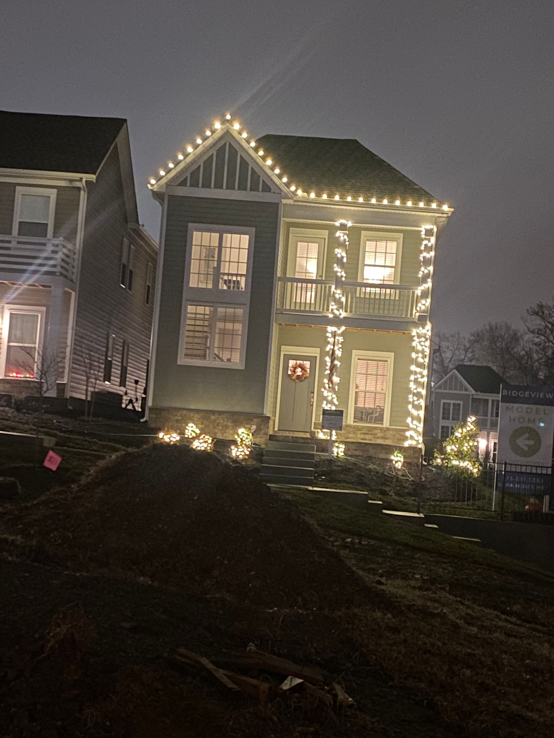 A two-story house decorated with white Christmas lights on a cloudy night.