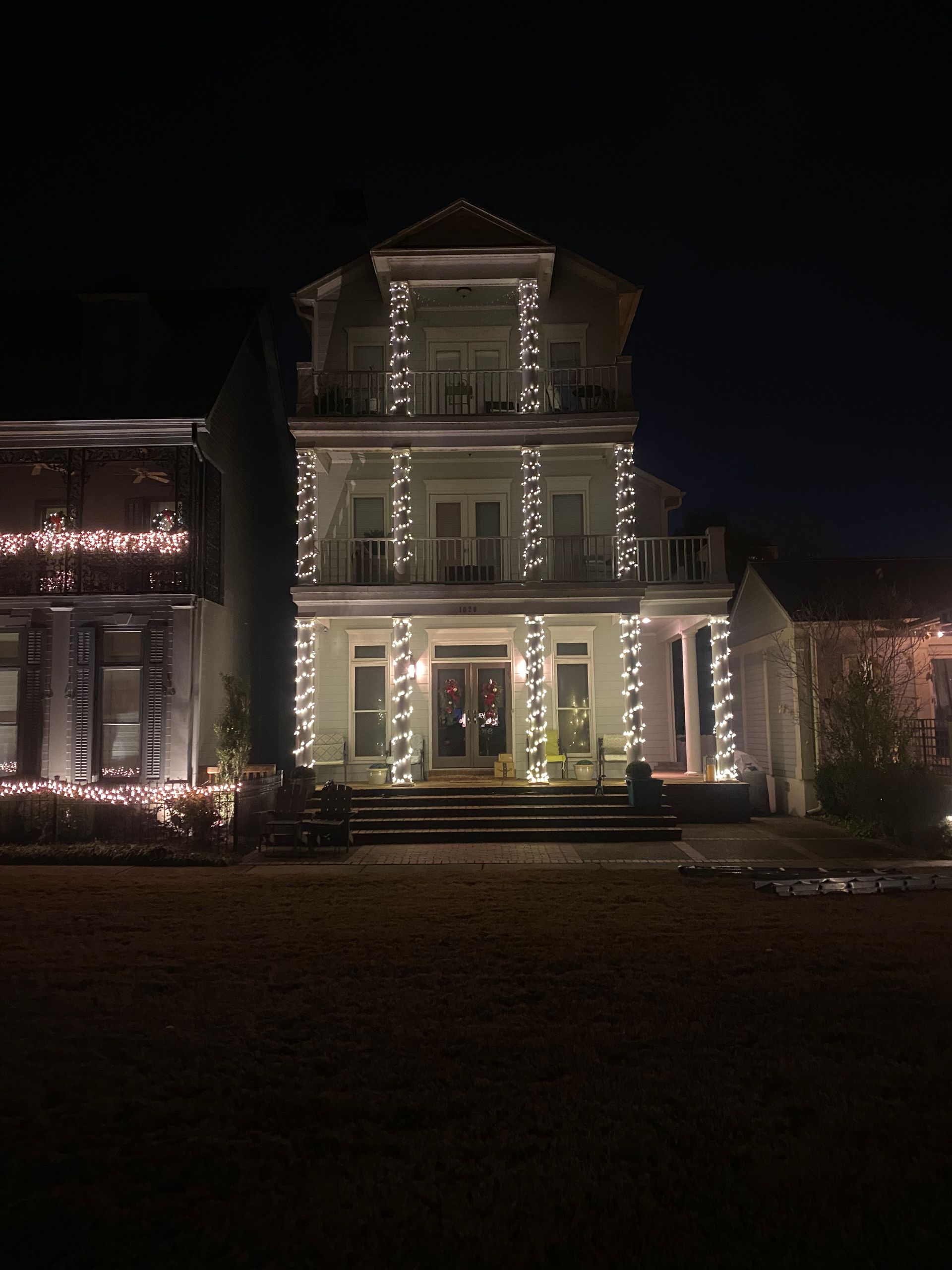 A three-story house at night, lit with white string lights outlining the facade.