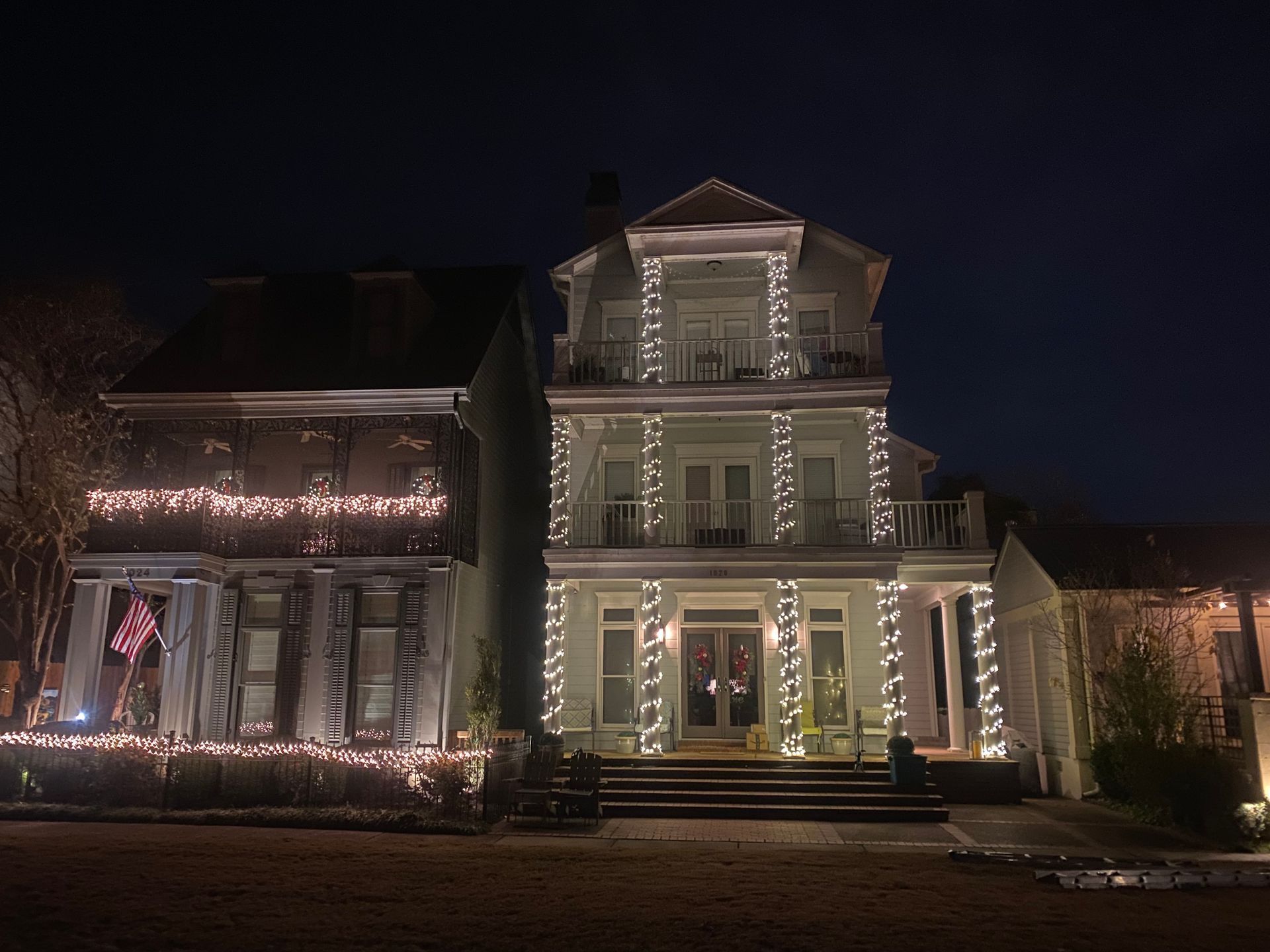 Two Victorian houses at night, decorated with strings of white Christmas lights.