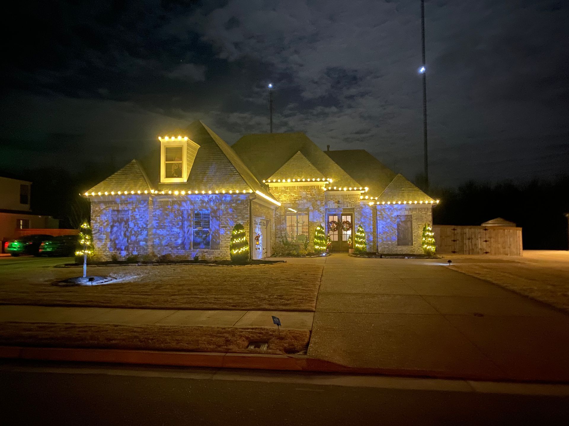 A house decorated with blue and gold Christmas lights at night. Two small lighted trees flank the front door.