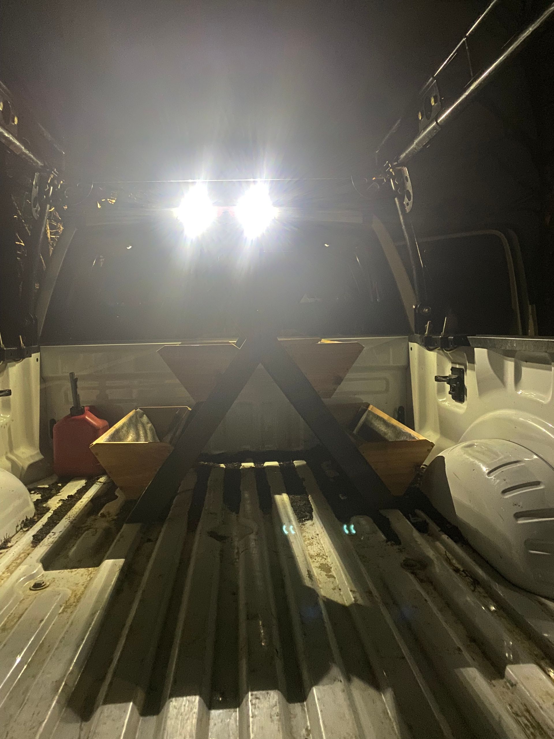 Inside a truck bed illuminated by overhead lights, a triangular frame with two yellow containers rests on the ribbed floor.