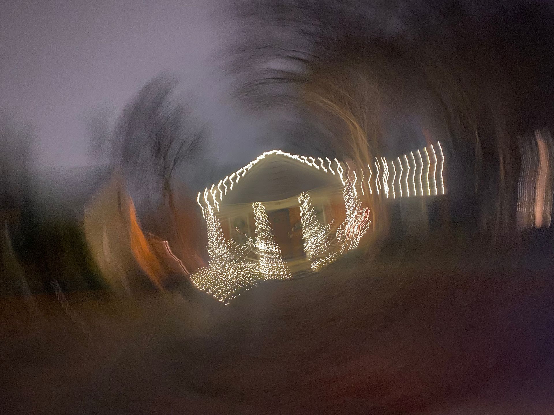 Blurred house with holiday lights, swirled effect, dark background.