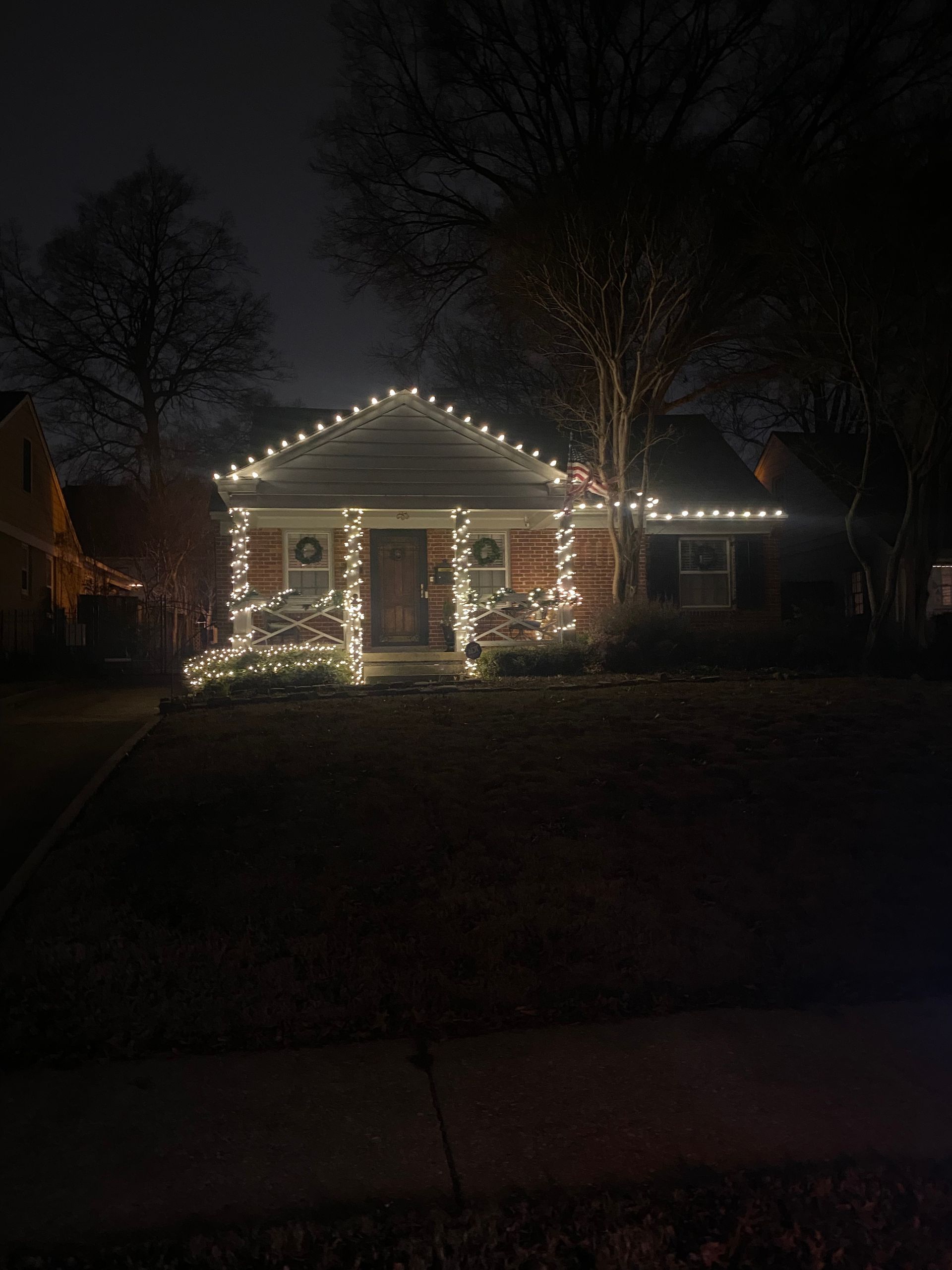 A house at night illuminated with white Christmas lights. Lights outline the roof, windows, and bushes.