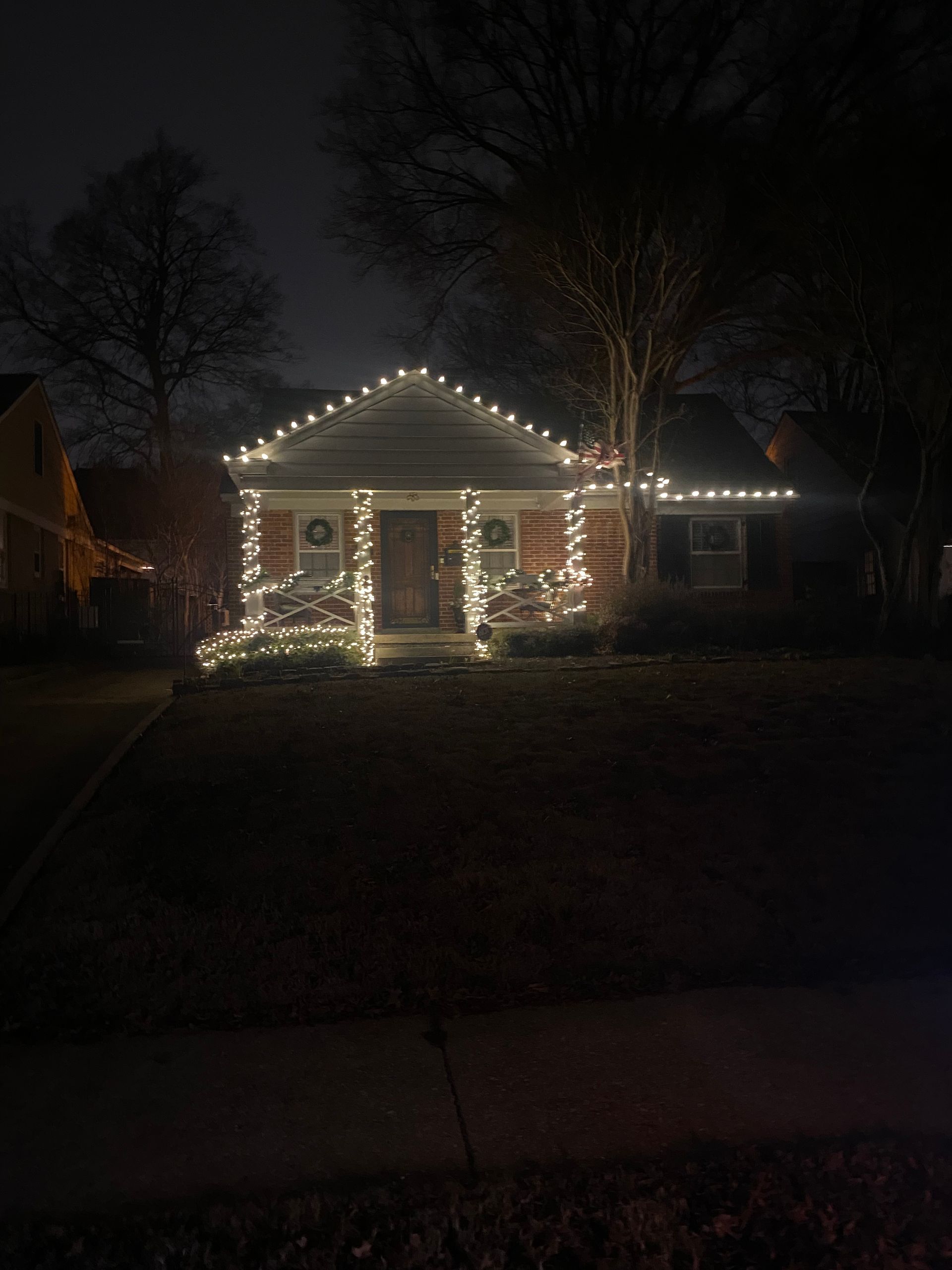 A house decorated with white Christmas lights at night. Lights outline the roof, bushes, and porch columns.