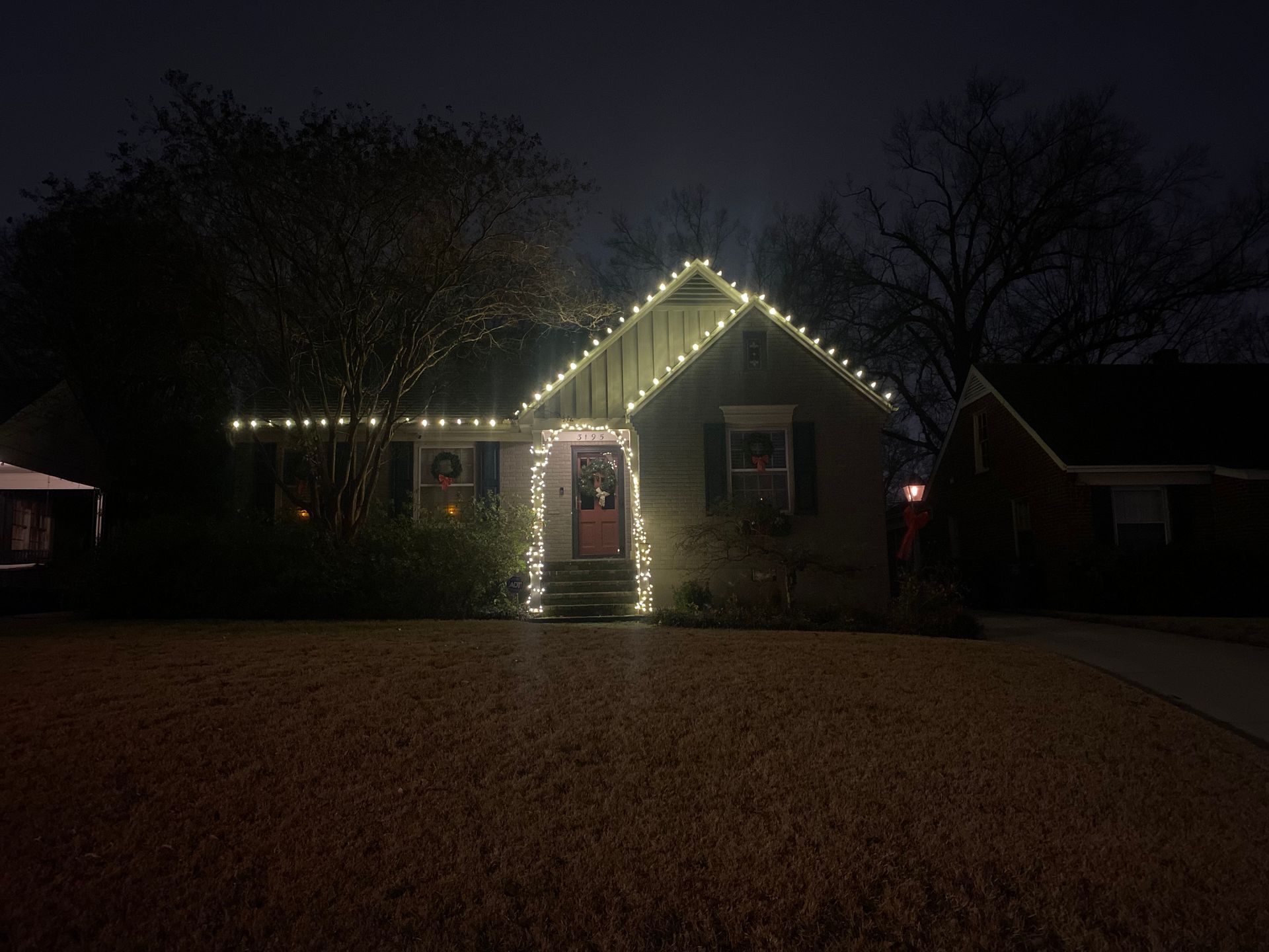 House at night decorated with glowing white Christmas lights along the roofline and around the front door.