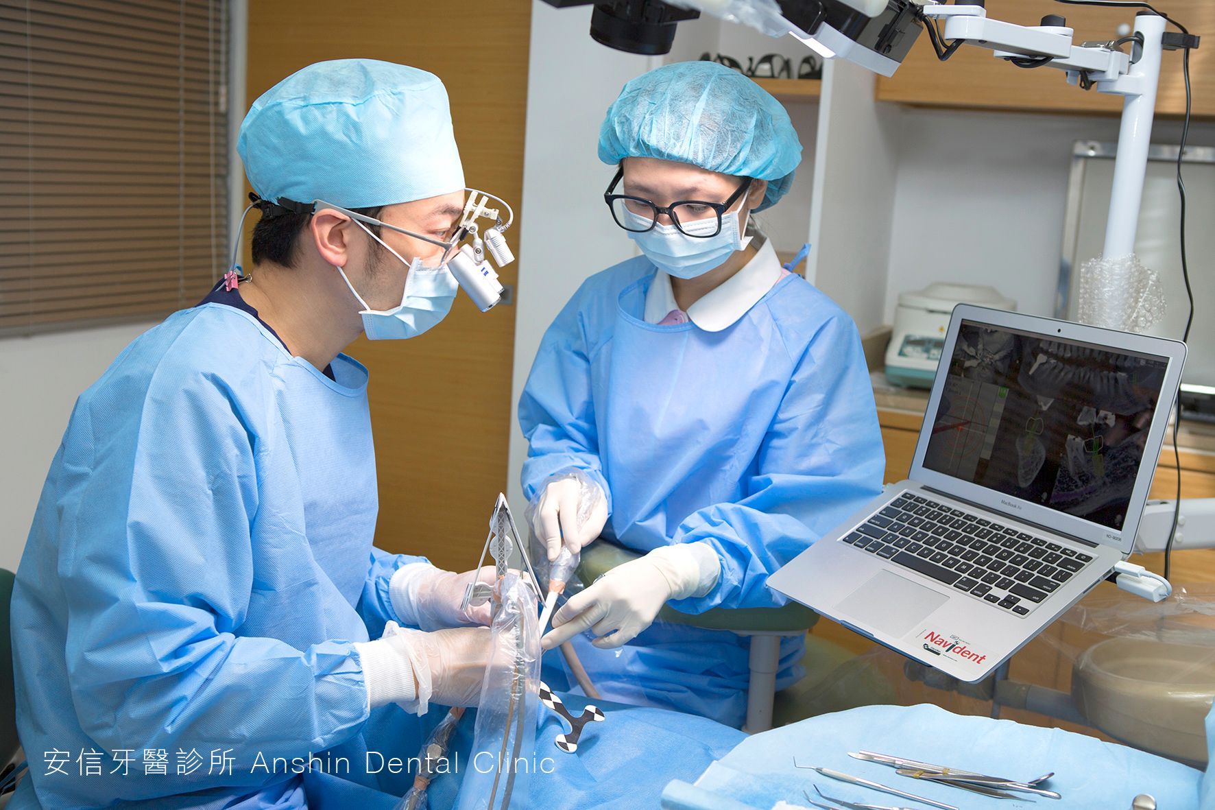 Two surgeons are working in an operating room with a laptop on the table.