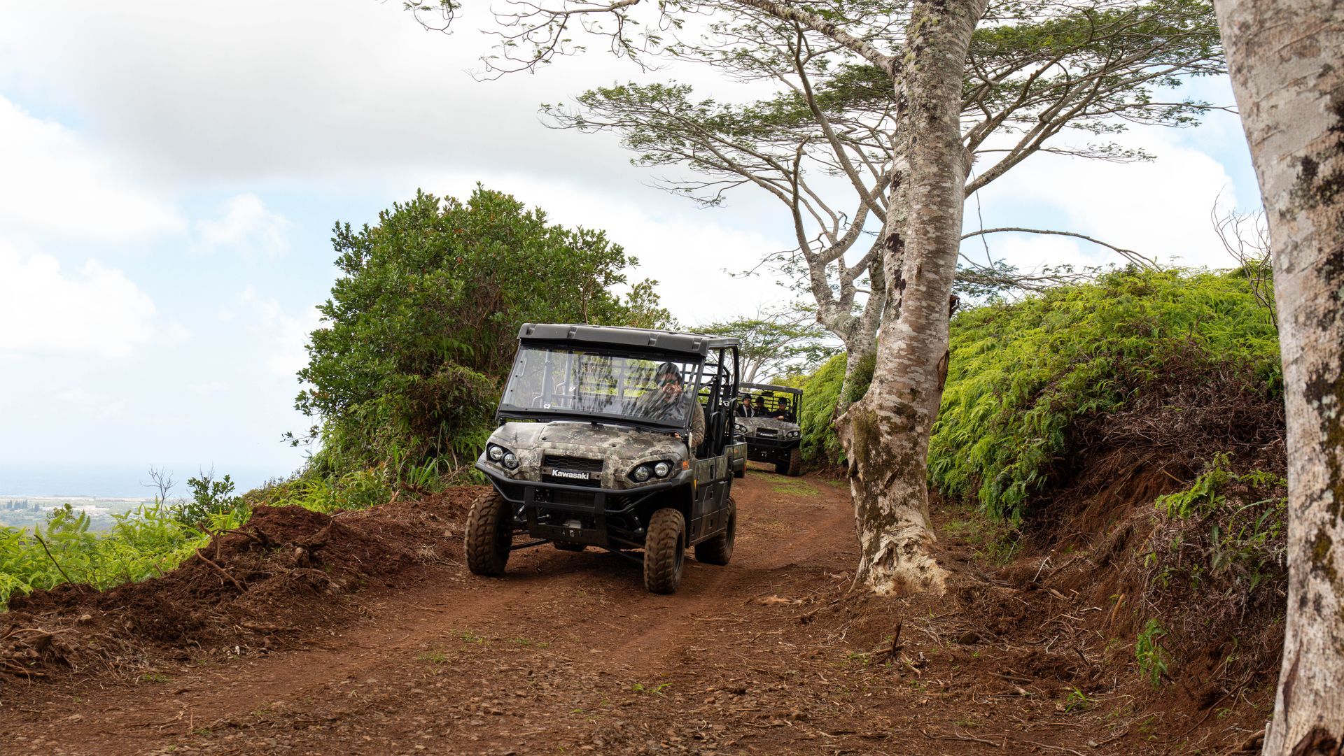 Off-road ATV on a muddy trail beside trees and bushes under a cloudy sky