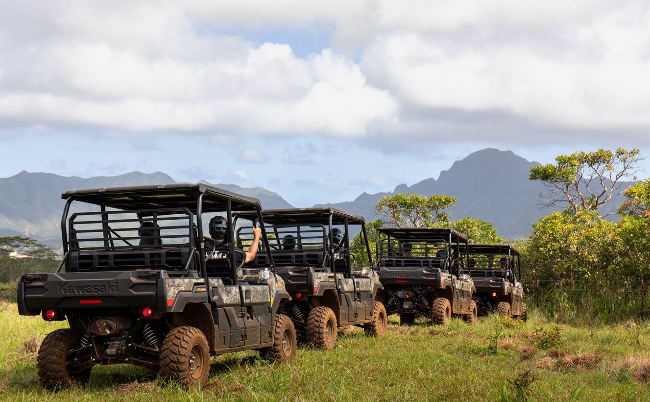 Four off-road safari vehicles parked in a grassy field with mountains and cloudy sky behind them