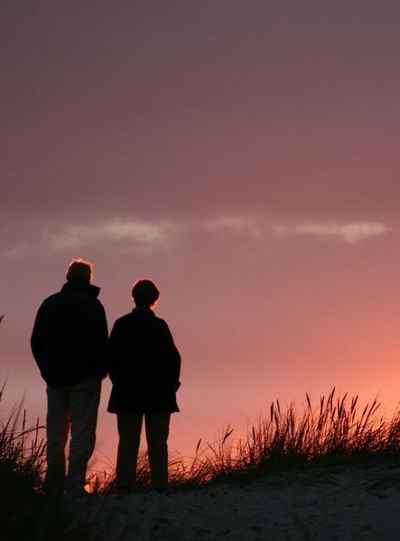 Two people are standing on top of a hill watching the sunset.