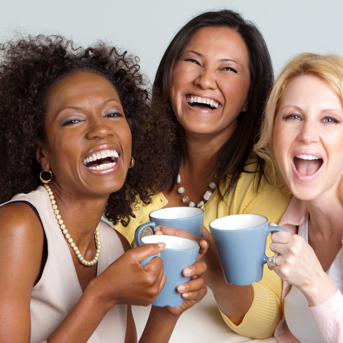 Three women are laughing and holding cups of coffee