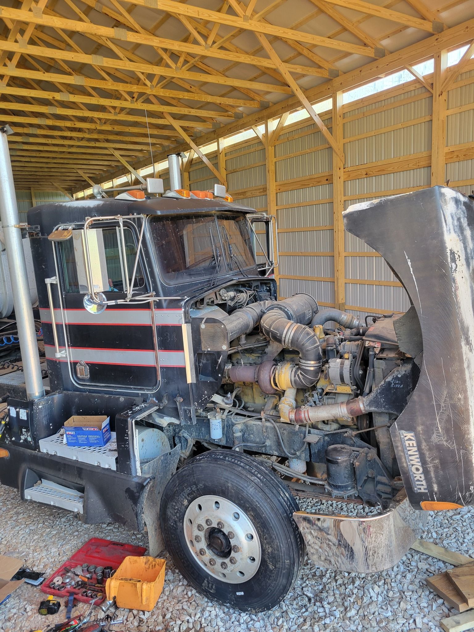 A truck with its hood open is sitting in a shed.