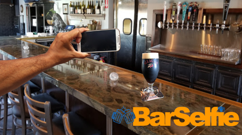 Hand holding phone, taking a photo of a dark beer on a bar counter at a bar with beer taps.