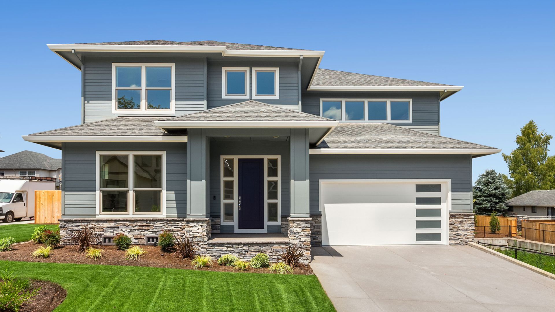 A large gray house with a white garage door is sitting on top of a lush green lawn.