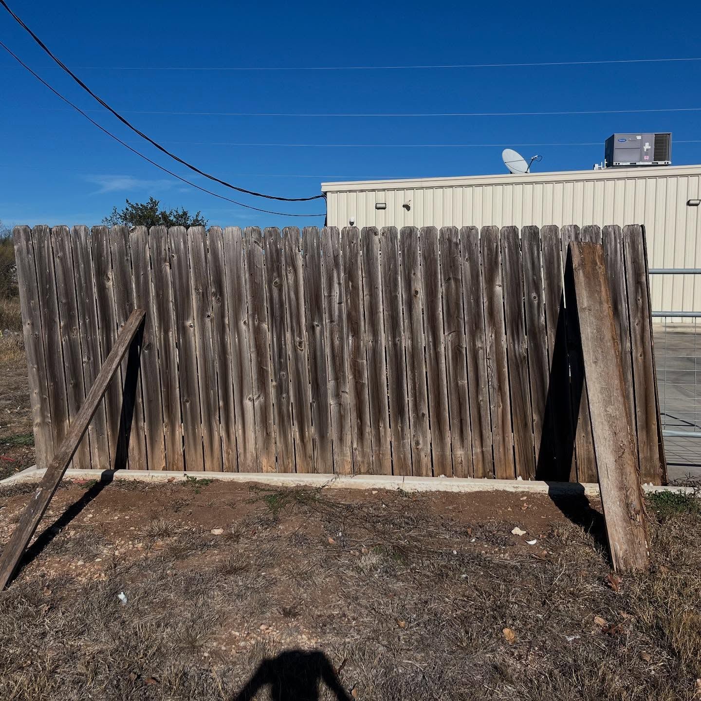 Weathered wooden fence with two supporting boards in a field with a building and blue sky in the background.