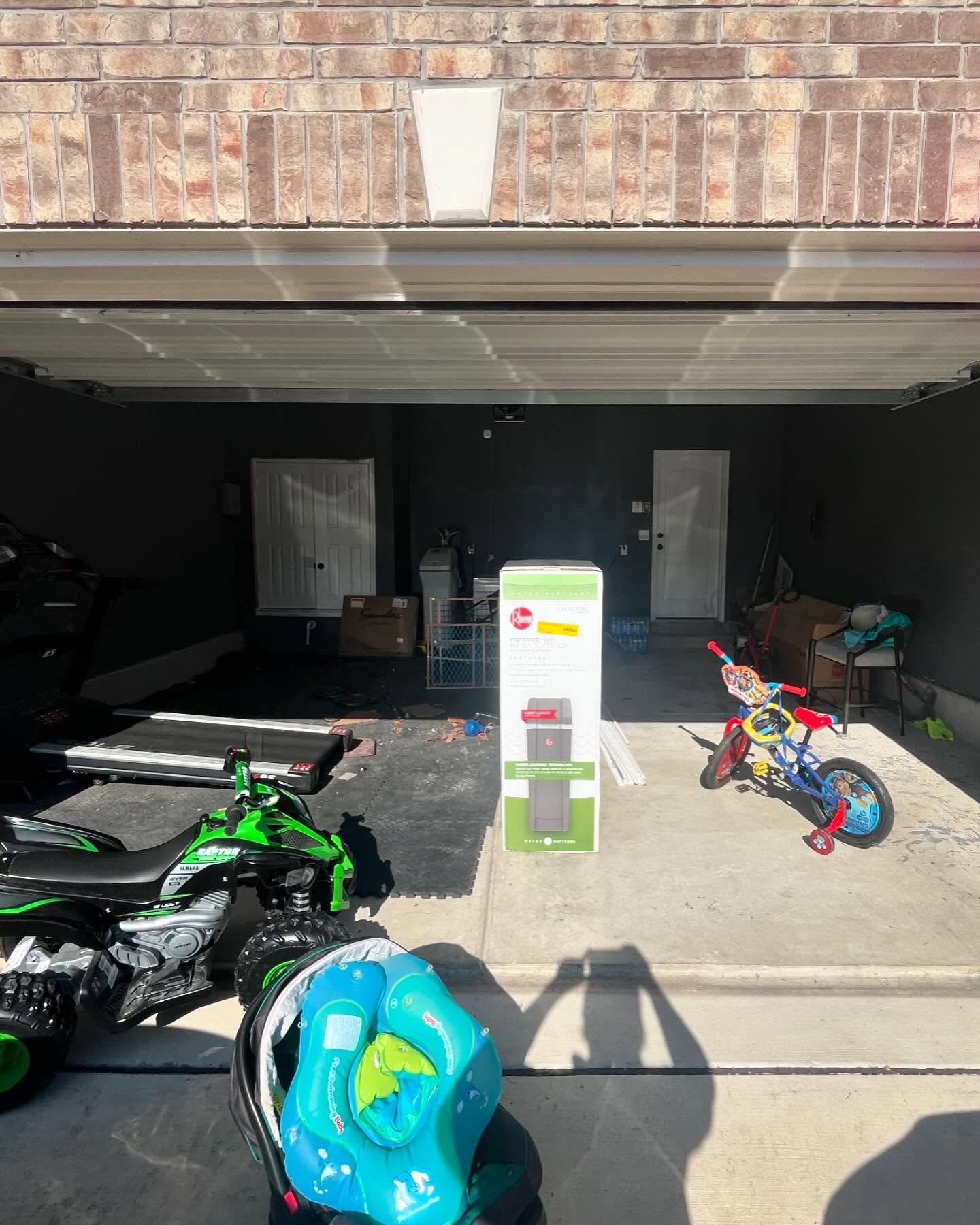 Garage interior with a green toy motorcycle and a child's tricycle. A boxed item stands near the center.