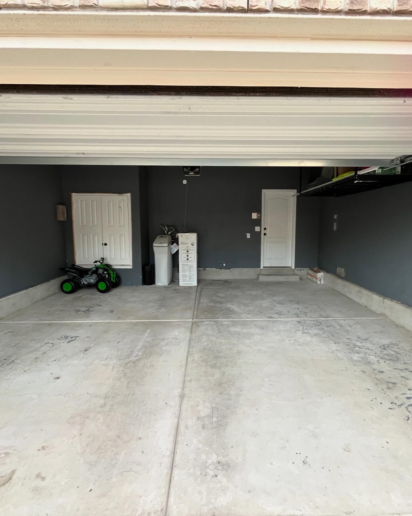 Empty gray garage with white doors, water system, and toy vehicle on concrete floor.