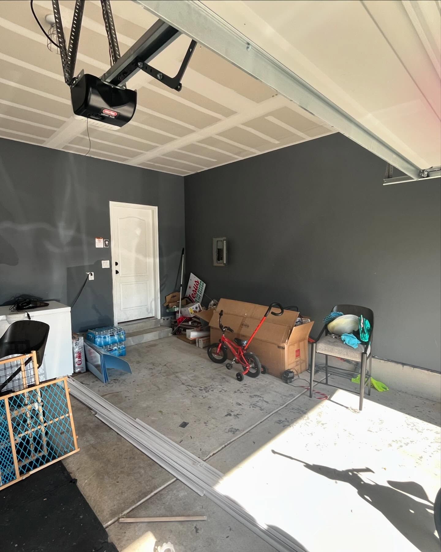 A garage interior with gray walls and a cluttered floor; a white door is visible in the back.